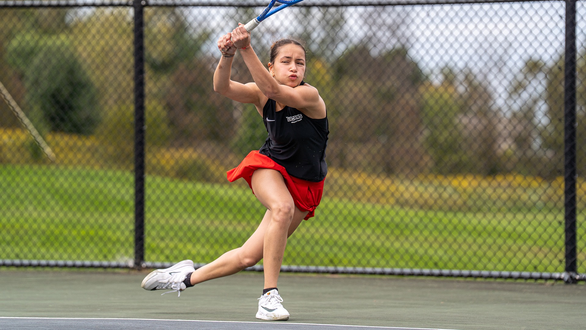 Tennis player Marion Sendra Lara stretches low across the court to hit a forehand return.