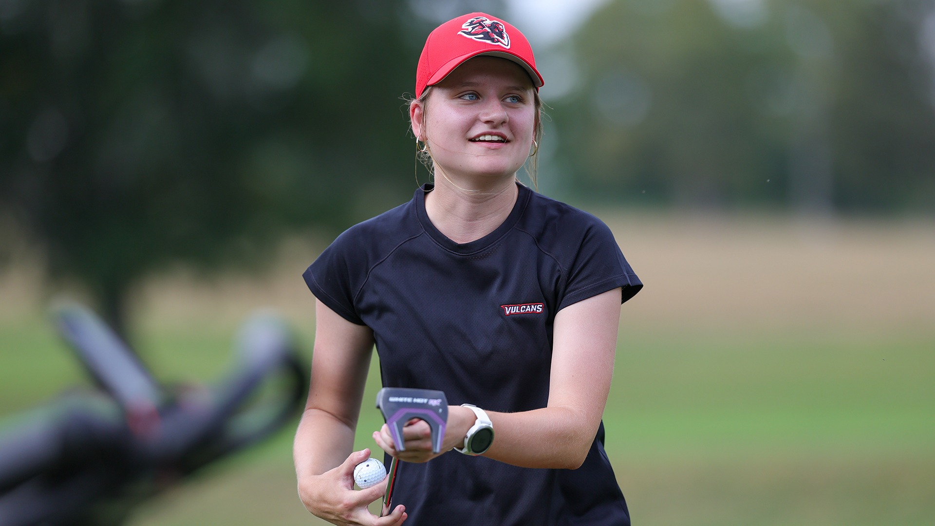 California golfer Amanda Woods smiling on the green with a putter and golf ball in hand.