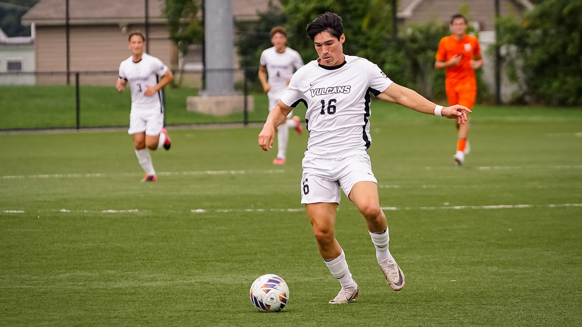 Soccer player Jaime Marcelo Espinosa (#16) dribbles a soccer ball down an outdoor turf field during a game.