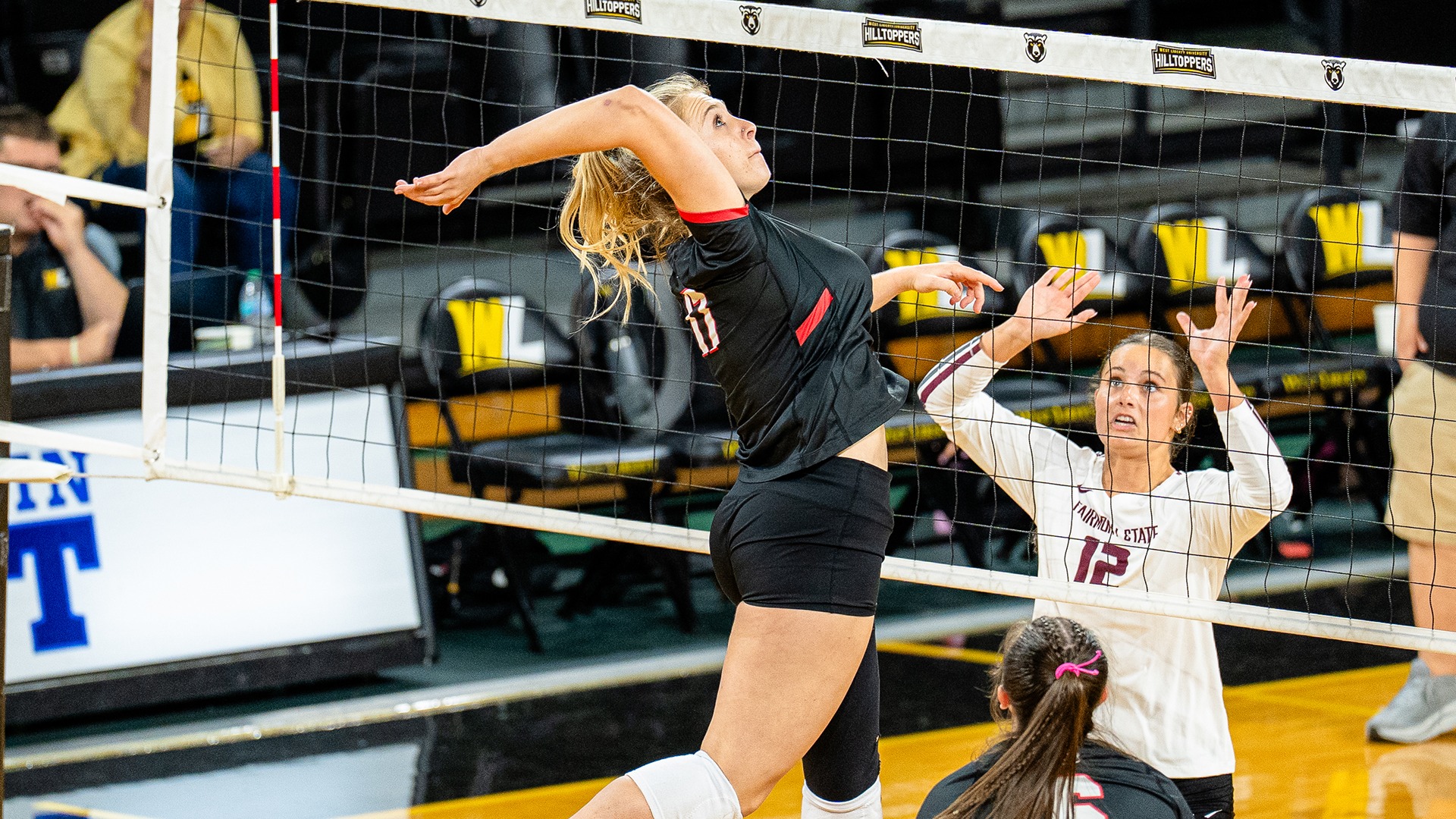 Lindsay Scammell jumps near the volleyball net to spike the ball while a Fairmont State defender reaches up to block.