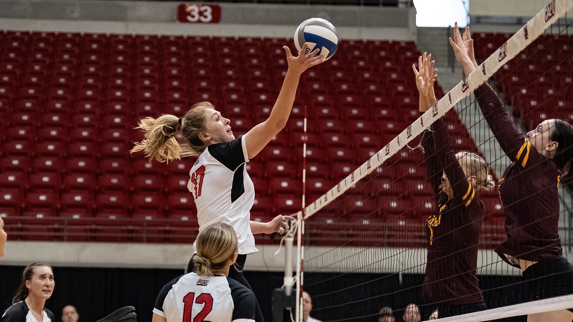 California volleyball player Lindsey Scammell leaps to tip a volleyball over the net past two opposing defenders attempting to block.