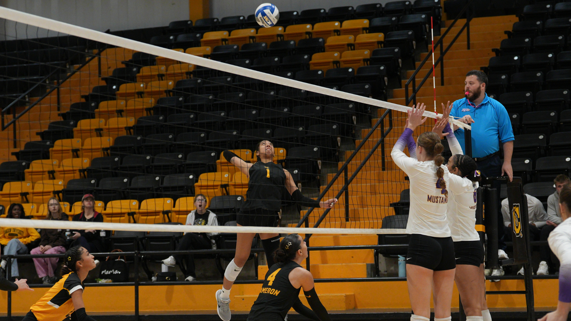 Cameron volleyball player No. 1 prepares to attack the ball as two opposing players jump to block at the net during a match inside Aggie Gym.