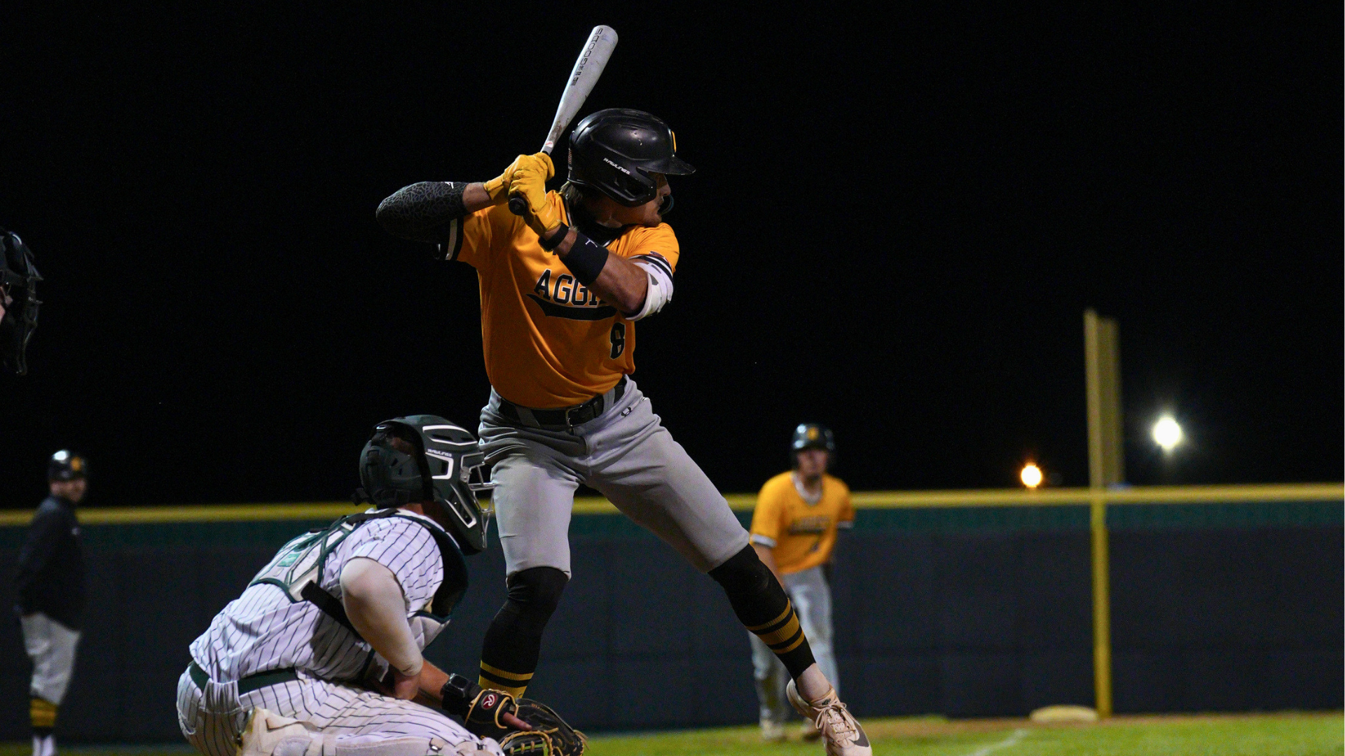 Baseball Player Zane Roos is at bat while opposing catcher waits for pitch. Another Aggie baseball player looks on from third base