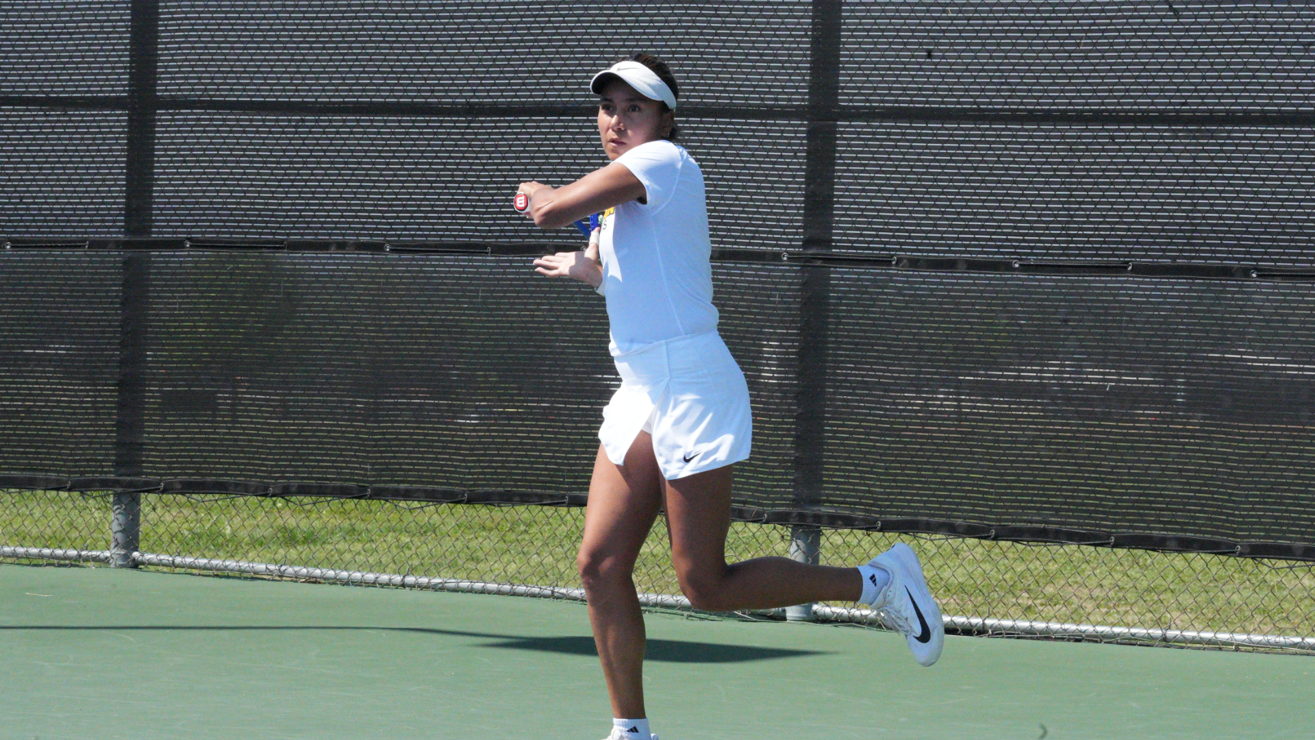 Cameron women's tennis player in white uniform hitting a backhand