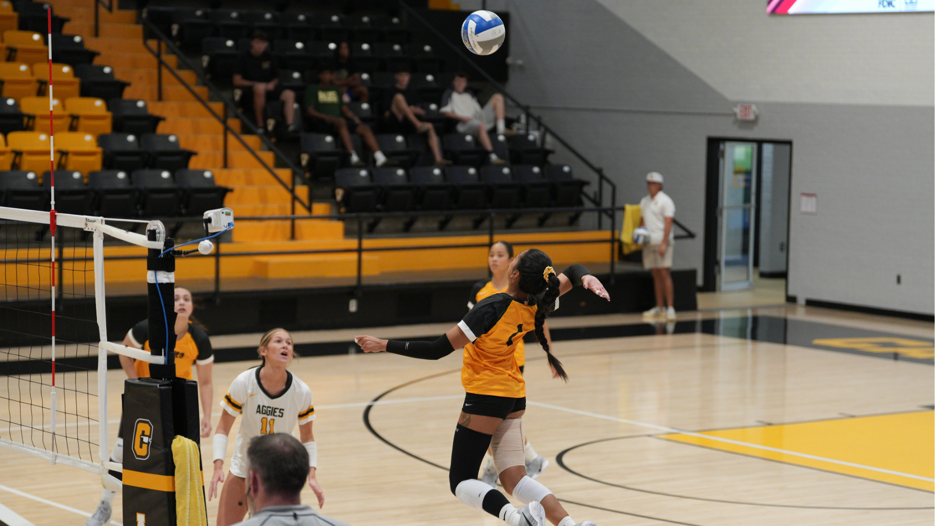 Cameron University volleyball player prepares to attack the ball near the net during a match inside Aggie Gym, with teammates positioned behind her on the court.