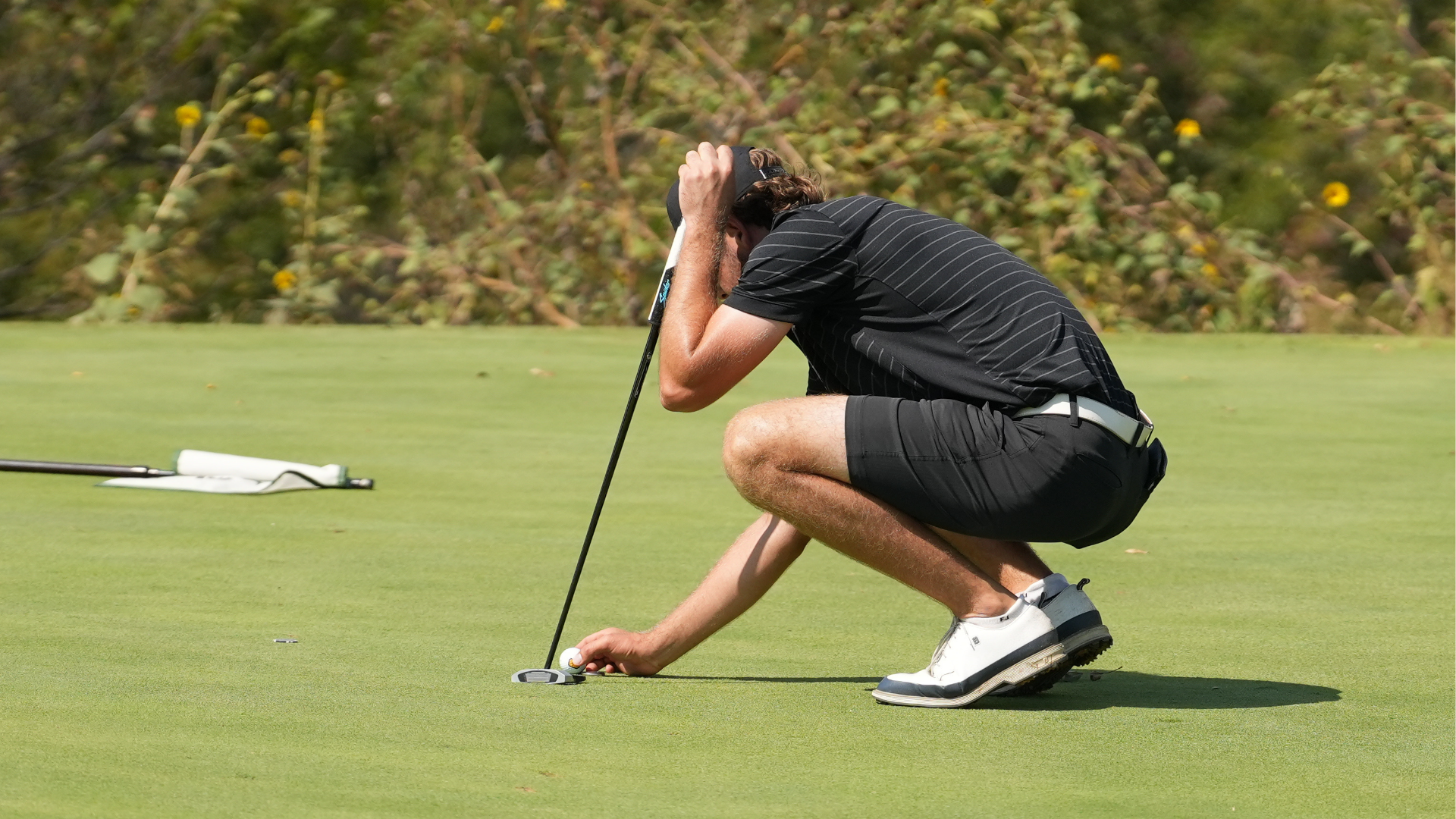 Cameron men's golfer kneels down to line up putt