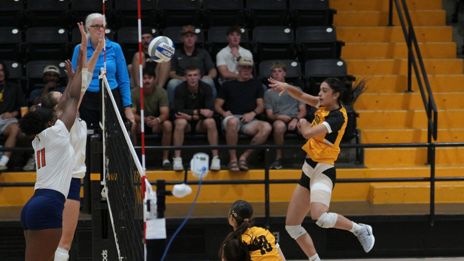 Cameron volleyball player attacks the ball near the net during a match inside Aggie Gymnasium as two opposing blockers defend the play.