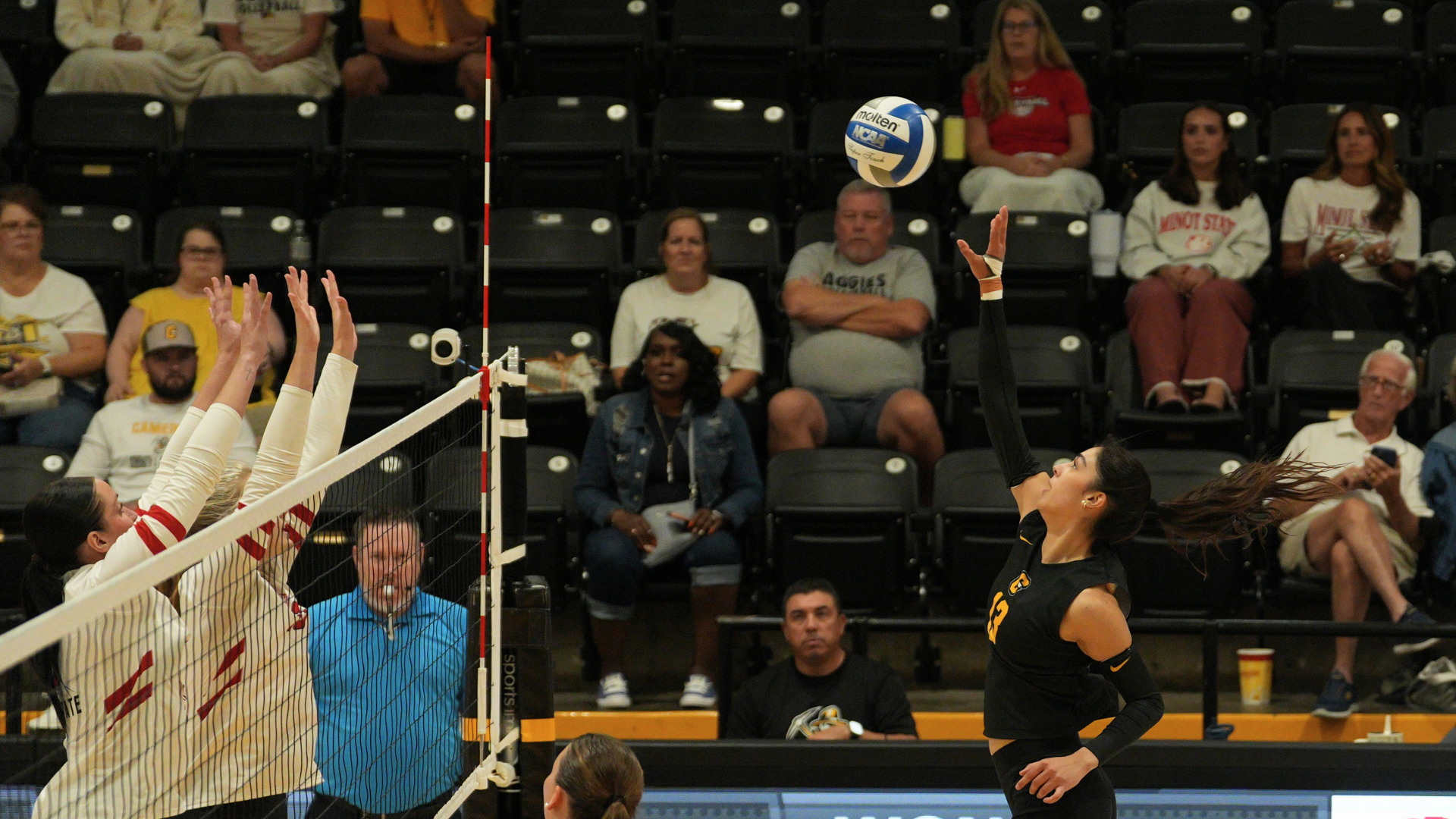 Cameron volleyball player attacks at the net against a pair of blockers during the Cameron Invitational at Aggie Gym.