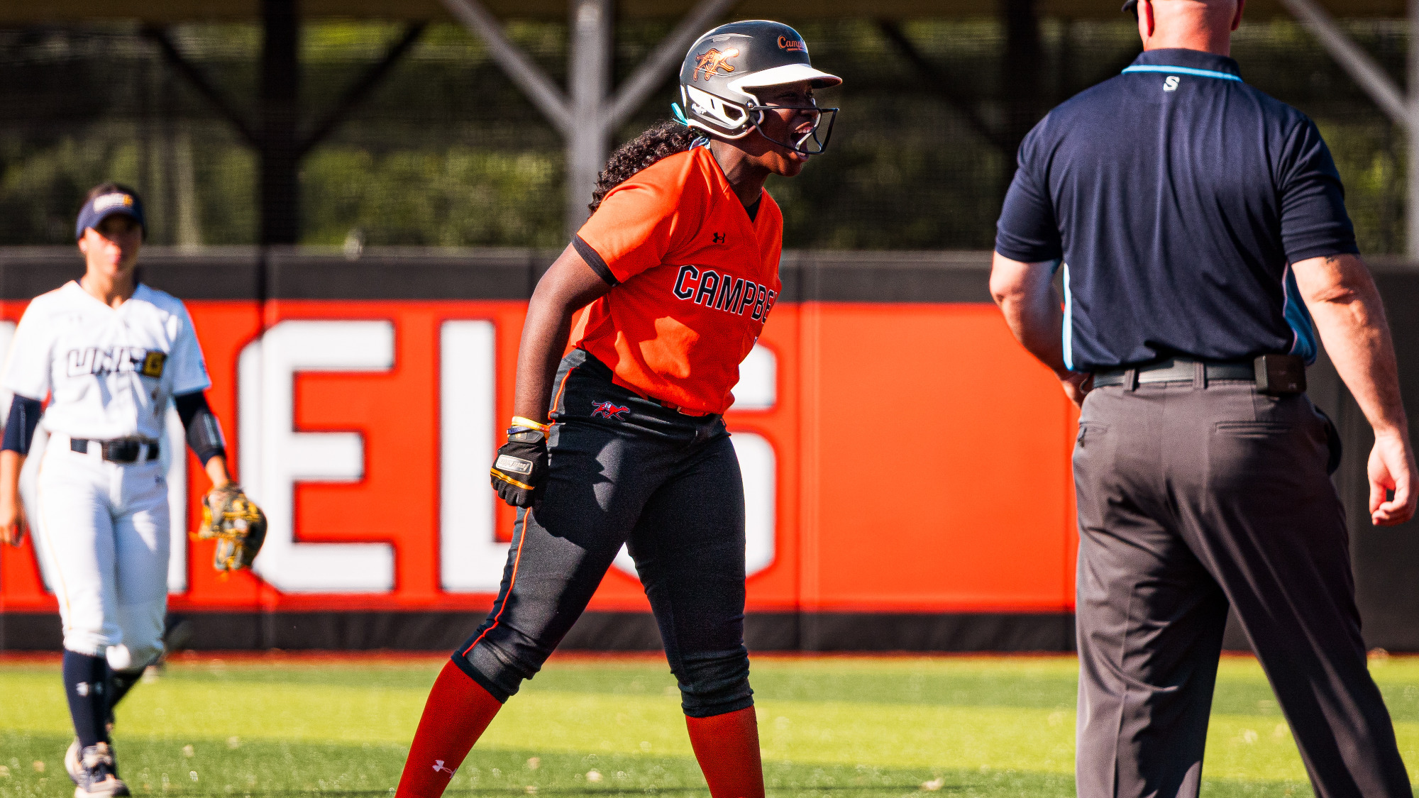 Allyiah Swiney in an orange jersey stands on second base, yelling in celebration.
