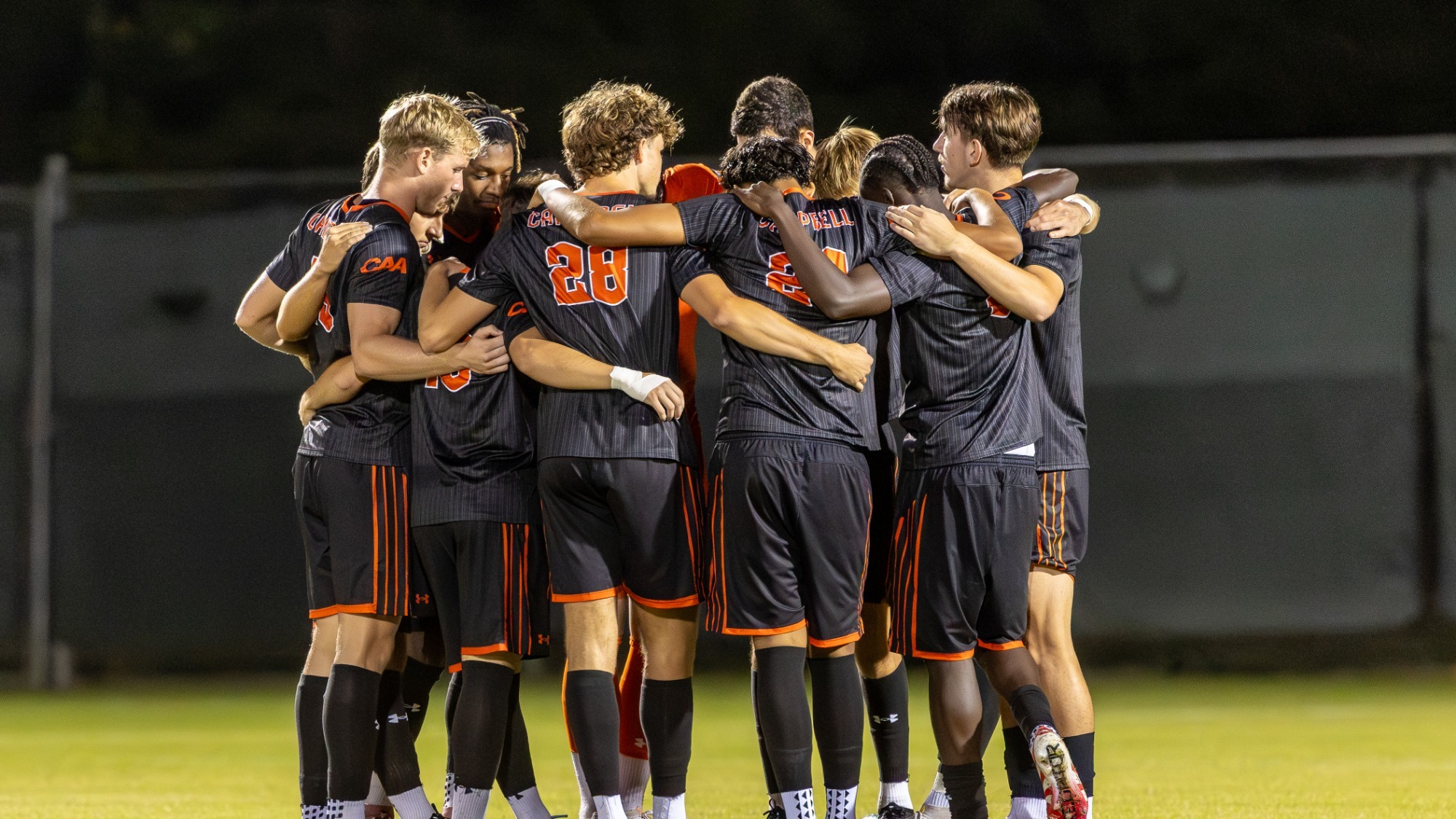 Campbell soccer players in black uniforms huddled together before a game with their arms around each other