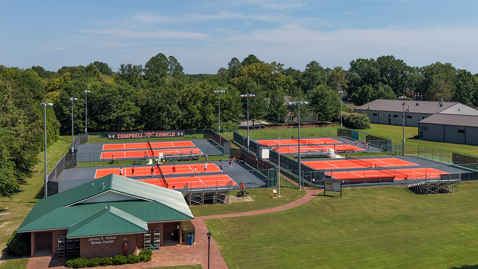 Aerial view of the Nisbet Tennis Center at Campbell University, featuring newly resurfaced bright orange tennis courts with gray surrounding areas and the tennis center building in the foreground.