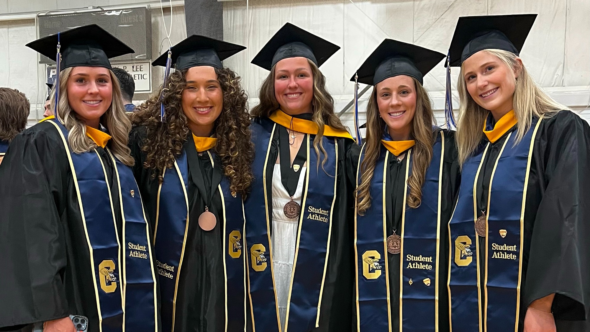 Members of the softball and women's lacrosse teams pose for a group photo in caps and gowns after spring graduation ceremonies