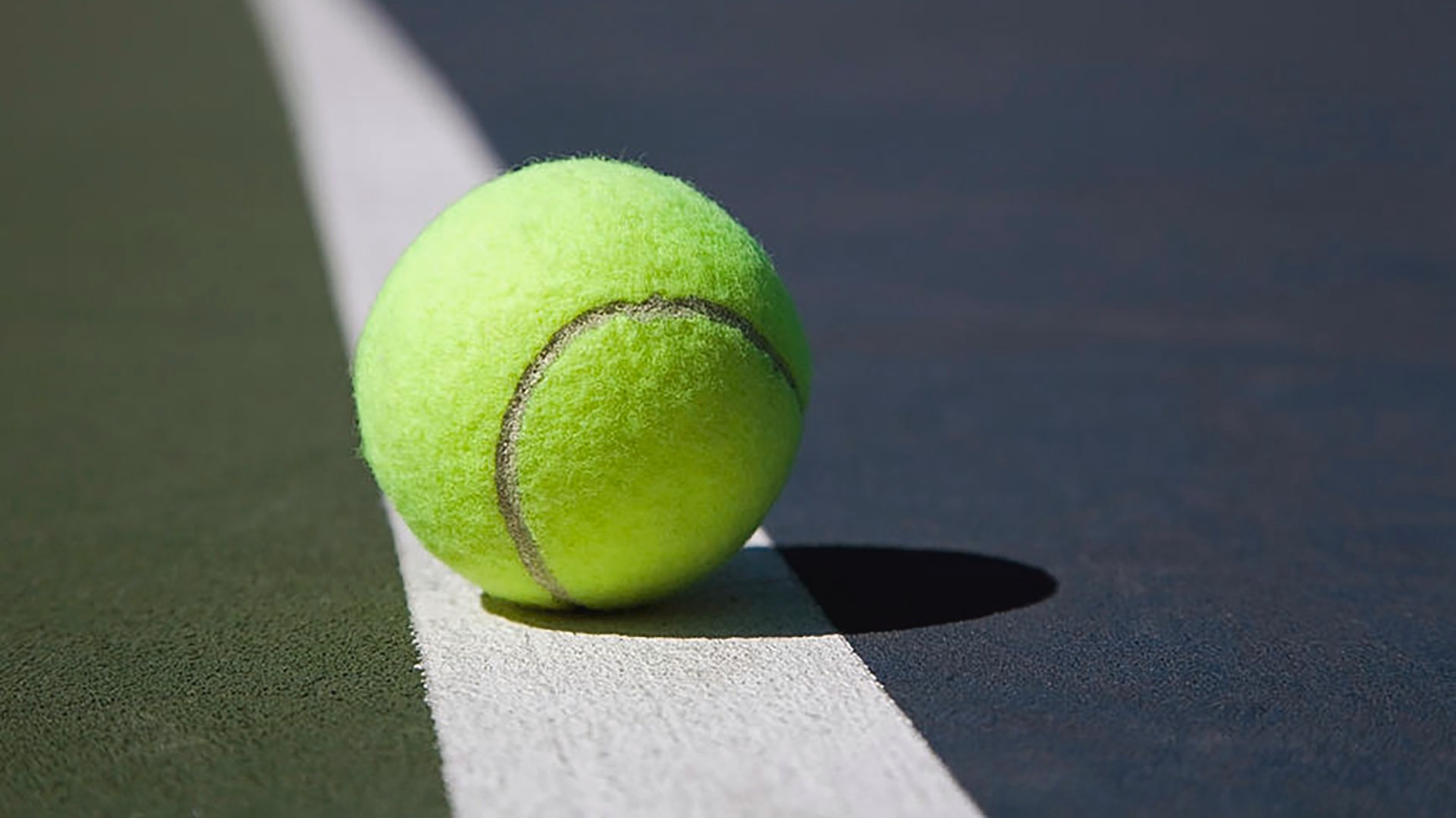 A tennis ball sitting on a hard court