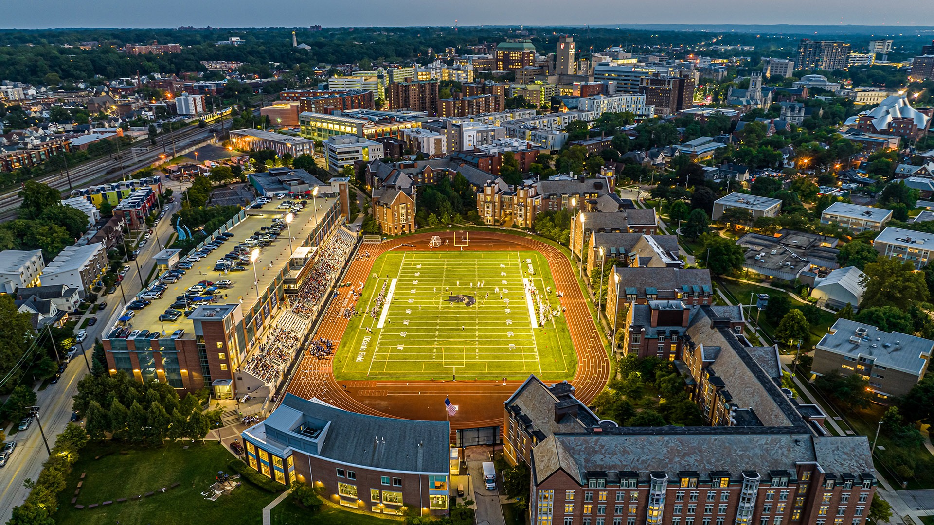 An aerial photo of DiSanto Field at night with the campus in the background