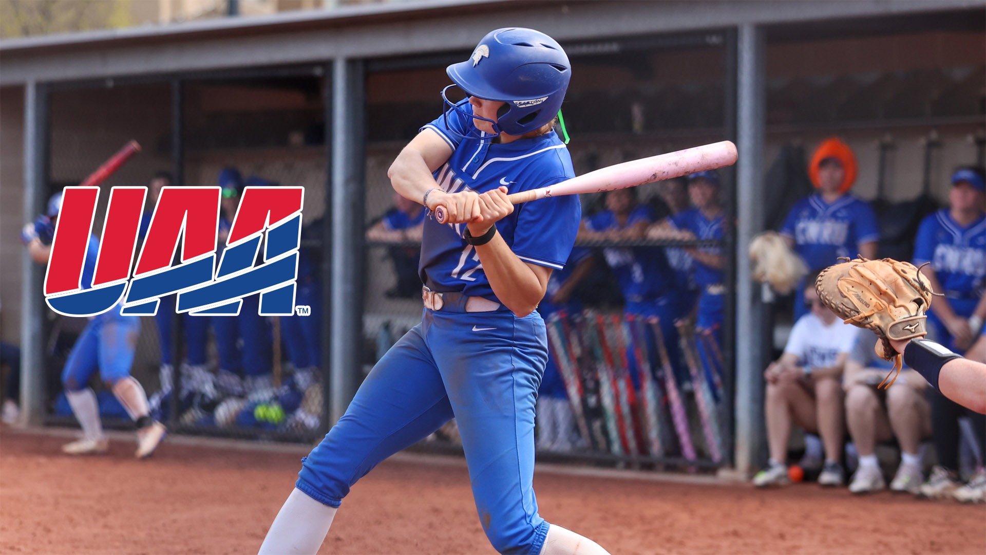 Karen Potts in the middle of a swing against Emory with the UAA logo middle left