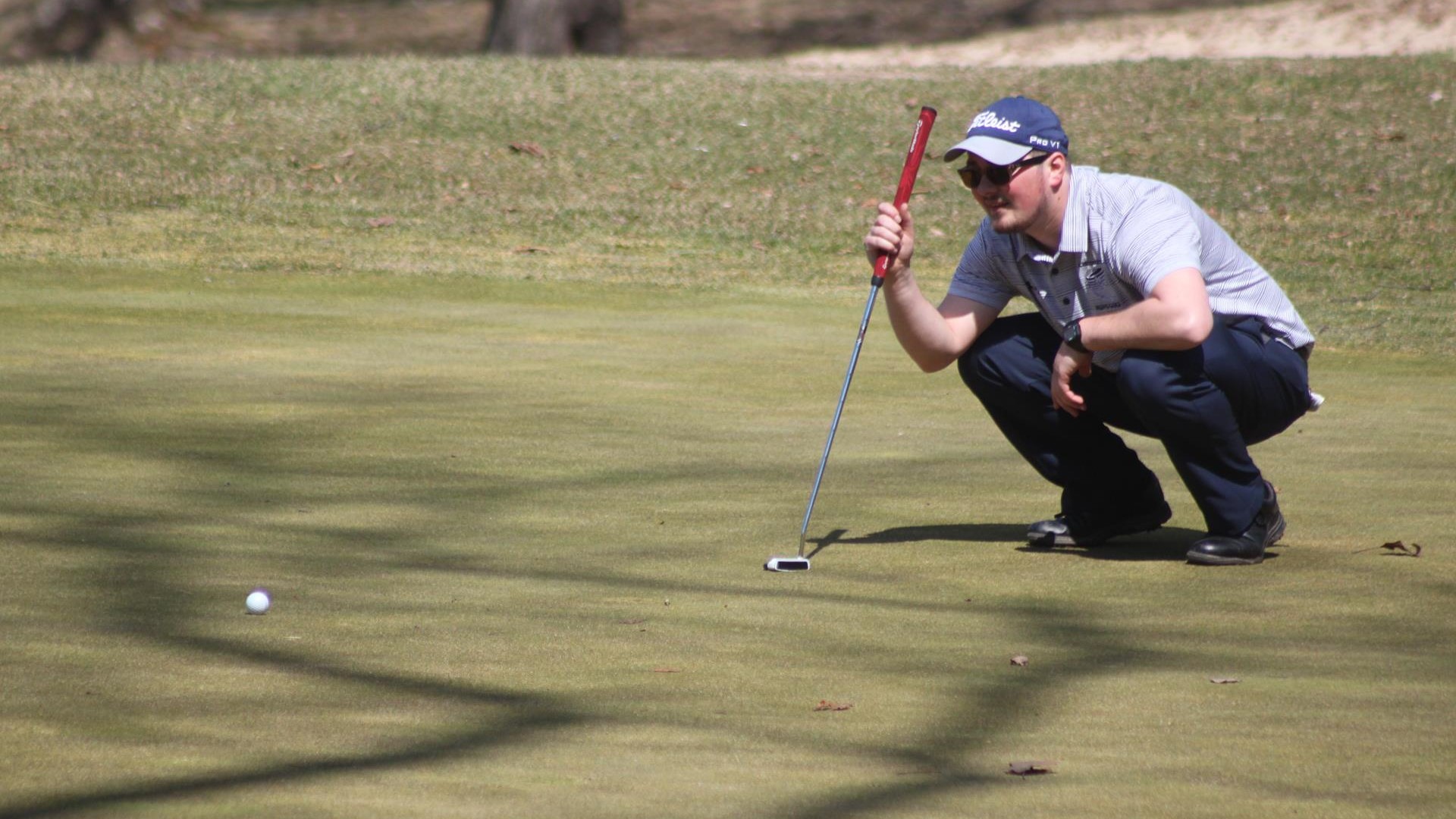 Tyler Bowman crouches over a ball with his putter resting on his shoulder
