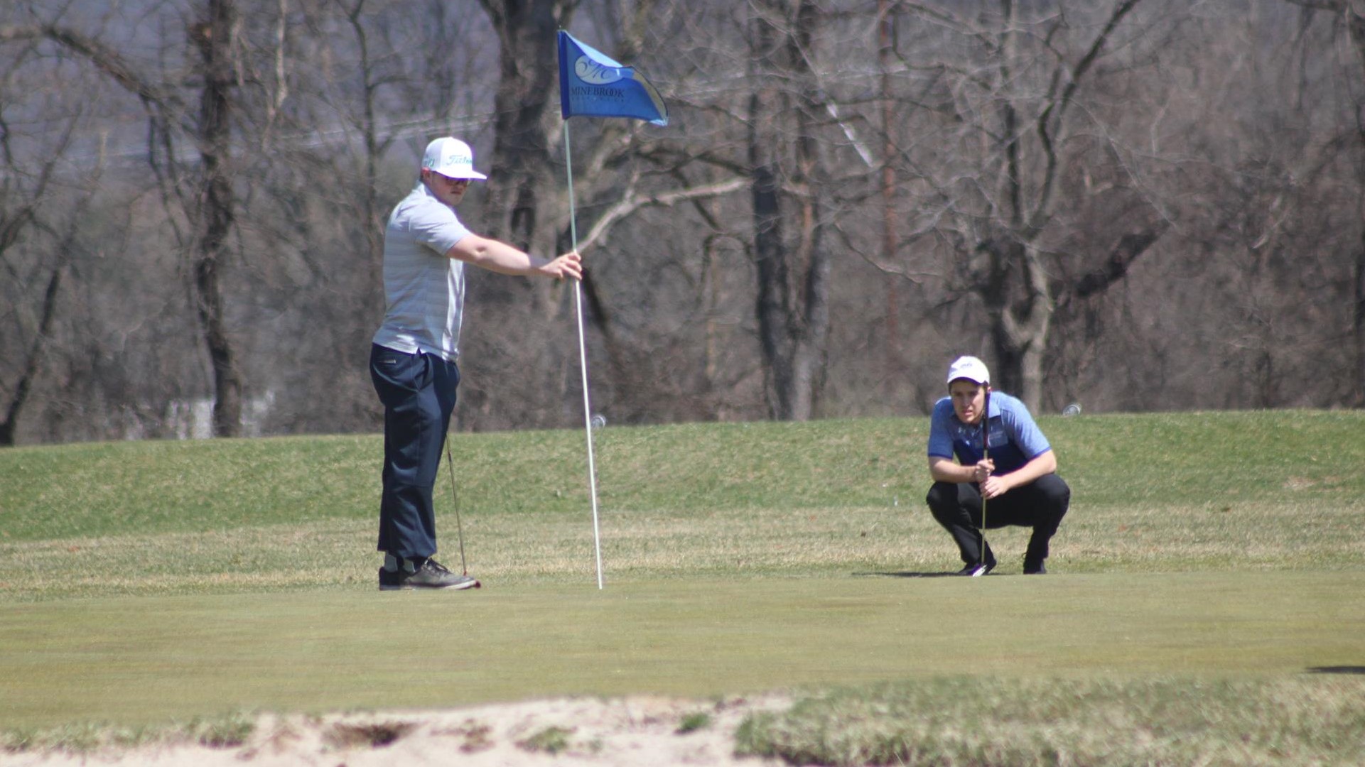 Jerome Beyer Jr. holds the flag stick on the green while an opponent looks over a putt