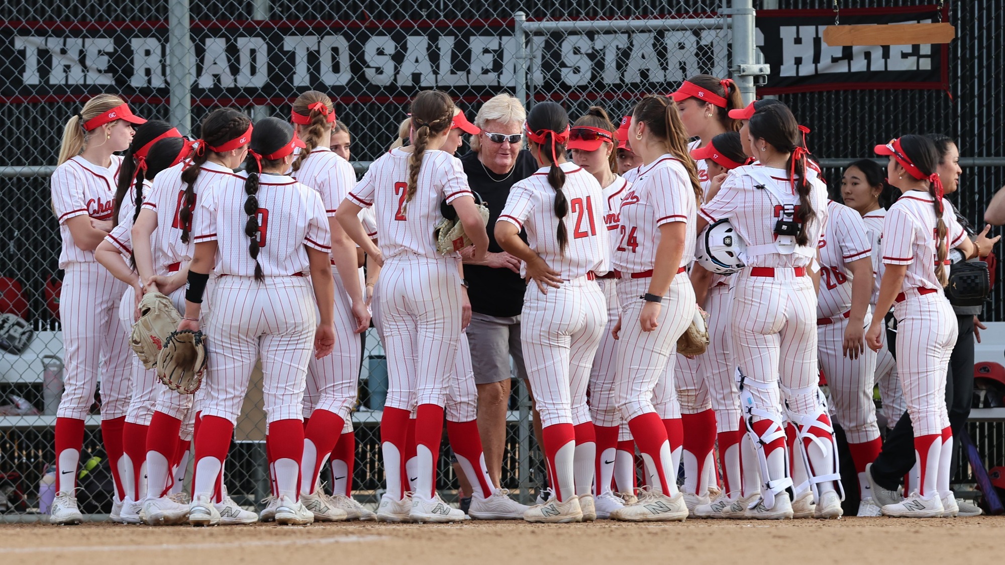 The softball teams huddles in front of the dugout. 