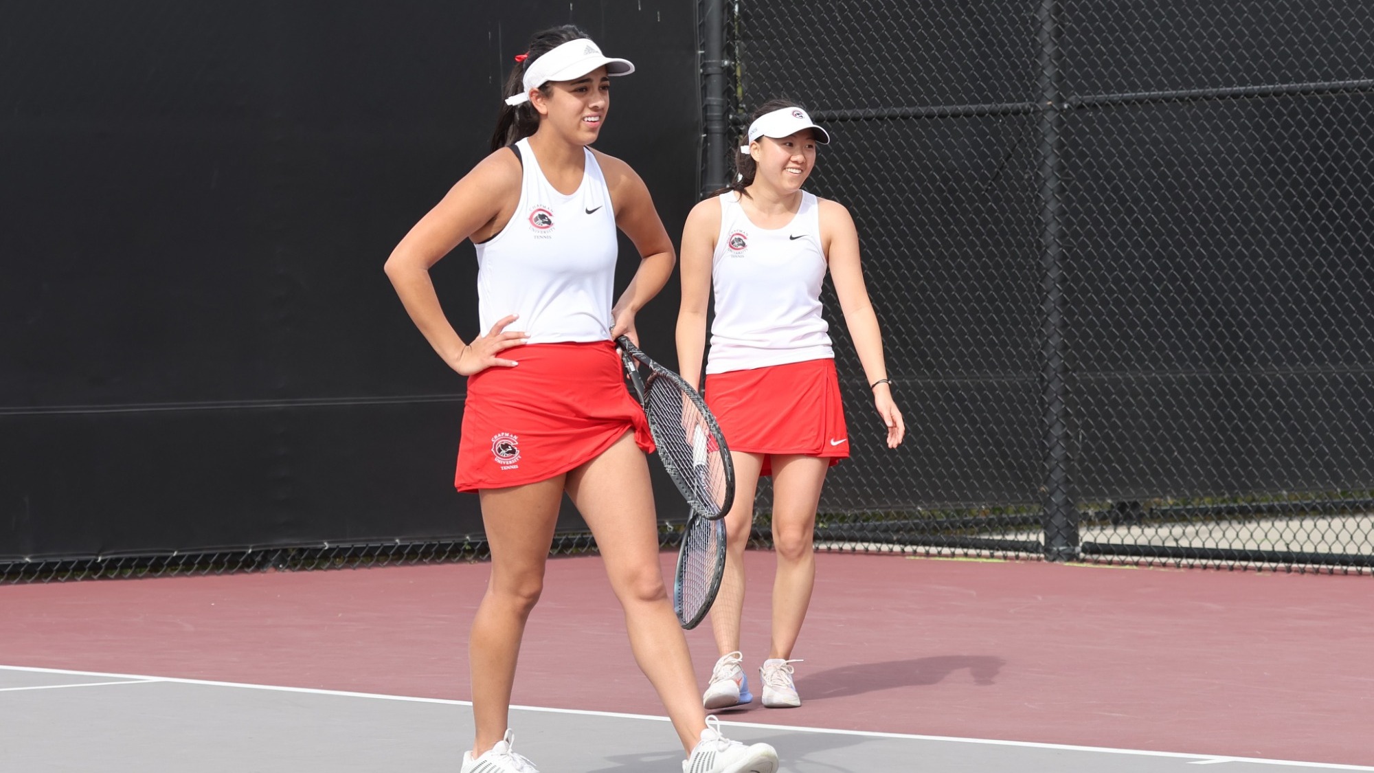 Sofiya Khegay and Jaya Manhas smile on the tennis courts after finishing a rally.