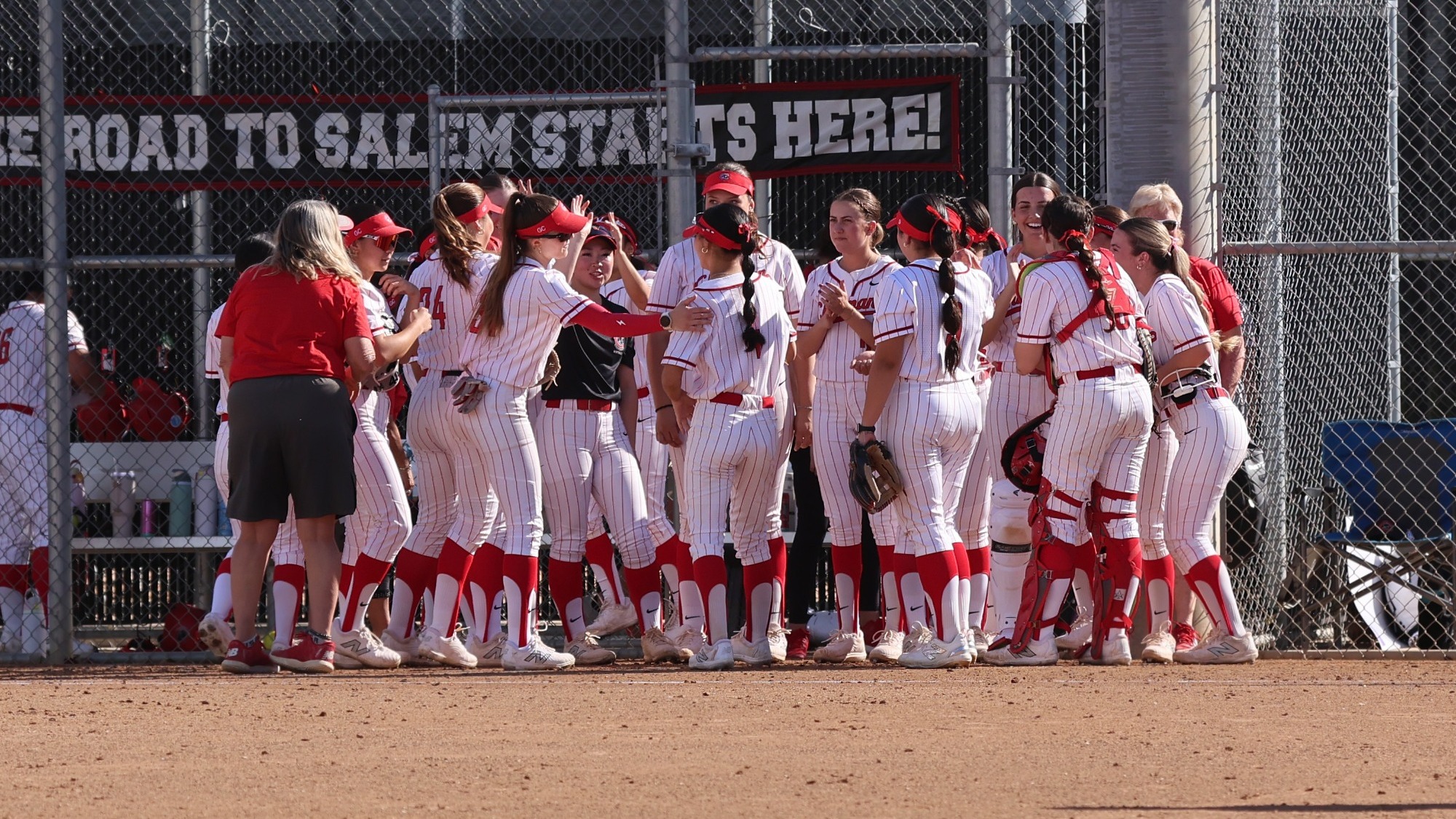 Softball team huddle in front of the dugout.
