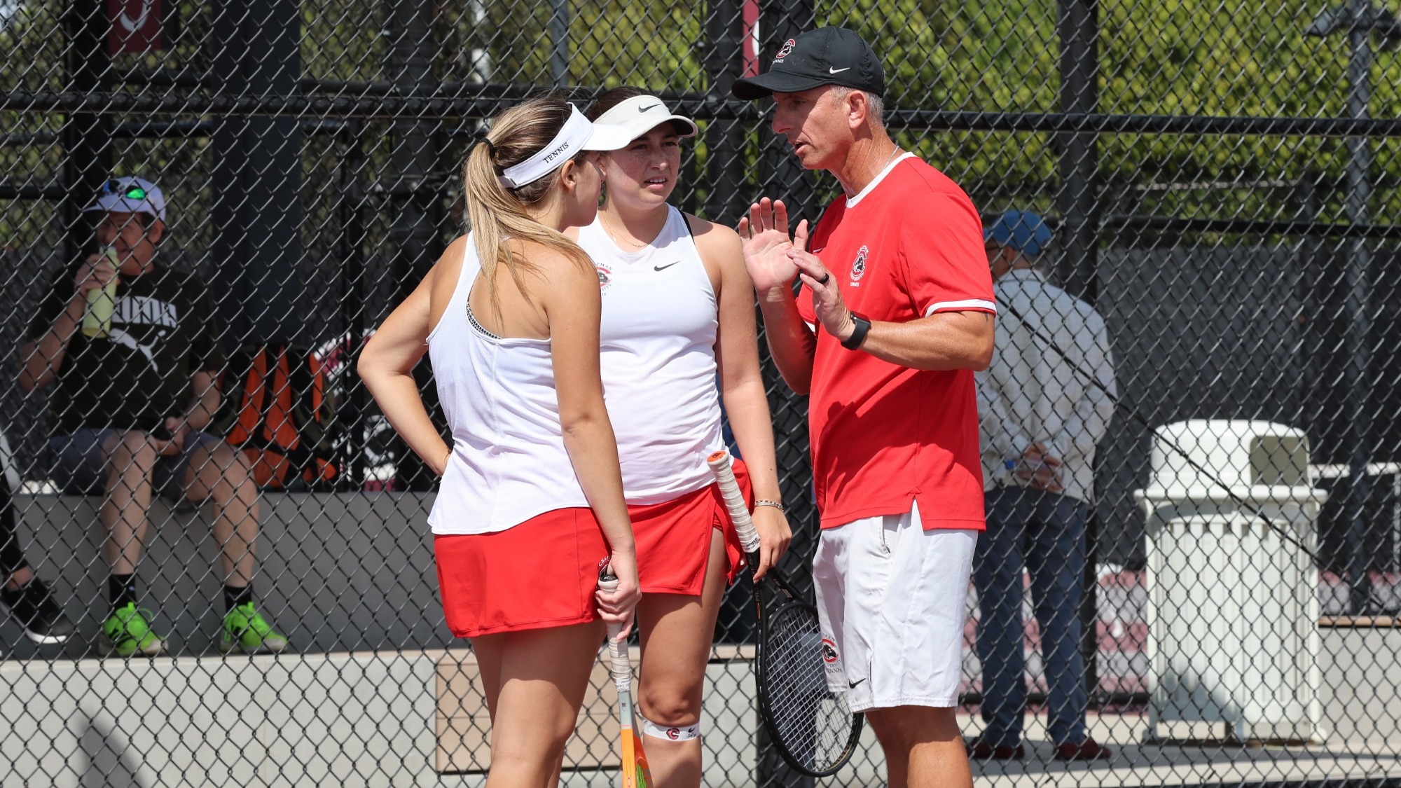 Head coach Evan Parry talks to tennis players on the court.