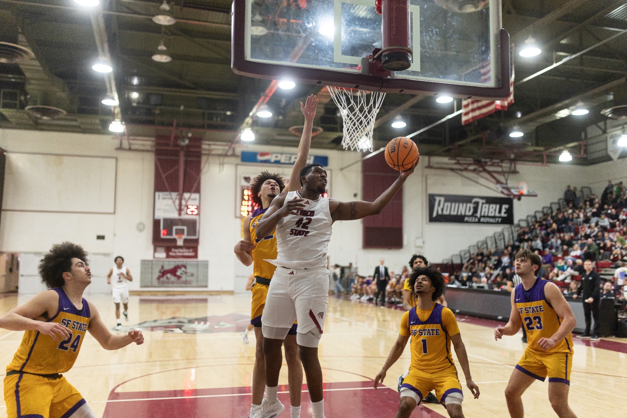 Isaiah Brewington lays up the ball from under the basket as a SF State player jumps to guard