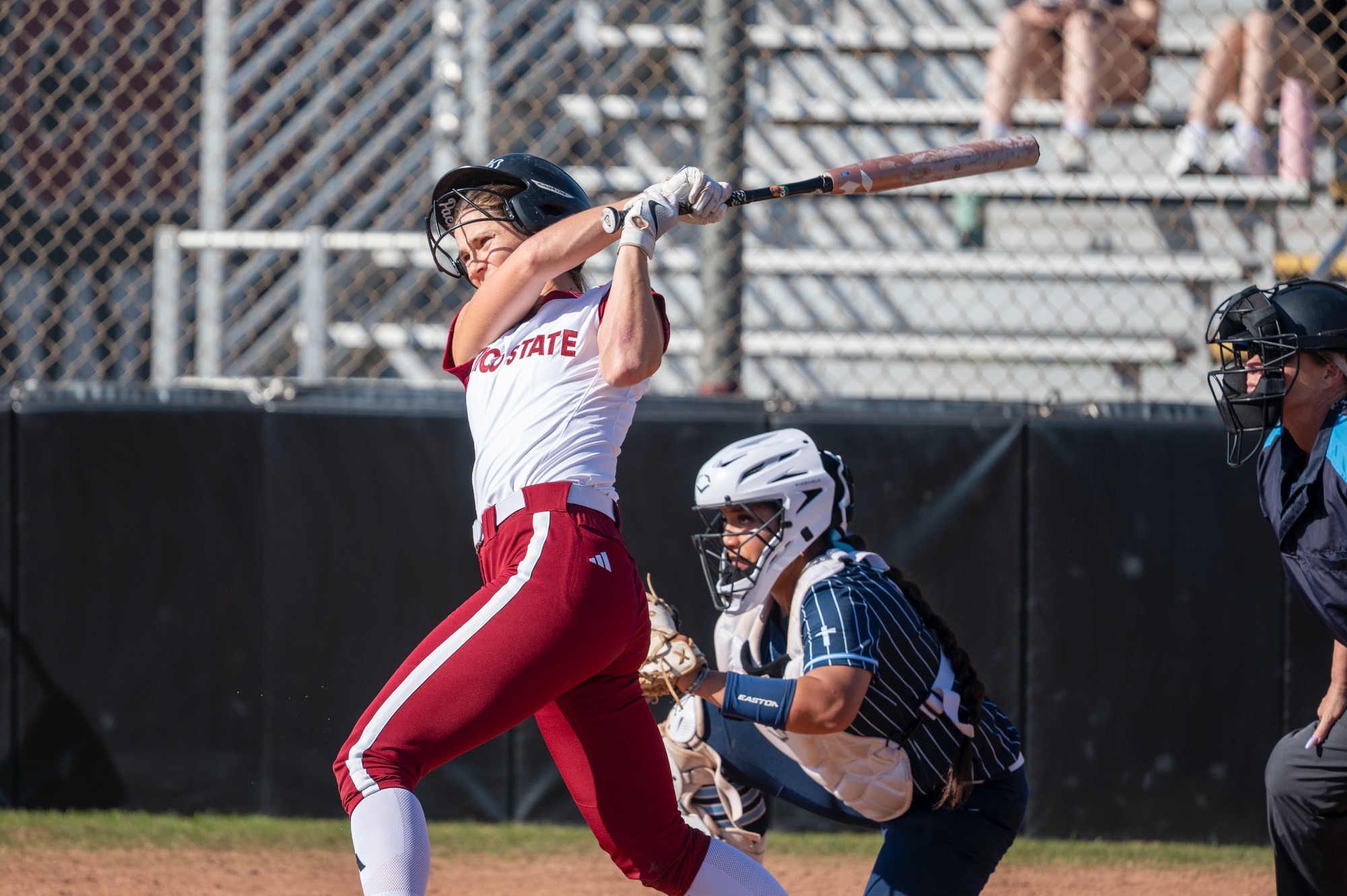Chico State softball player swinging at a pitch with helmet flying off