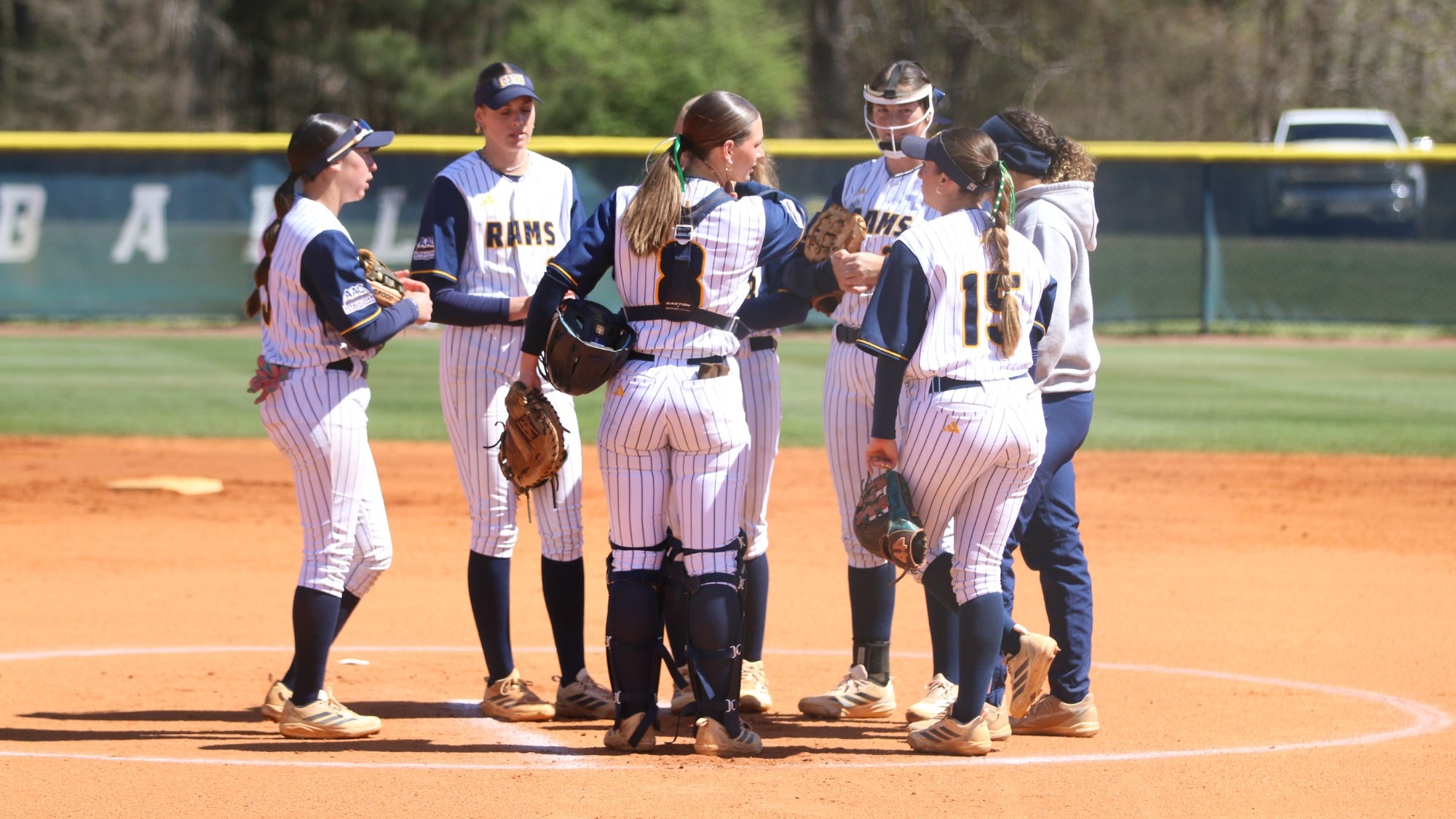 Softball team huddles at the pitching mound in between innings