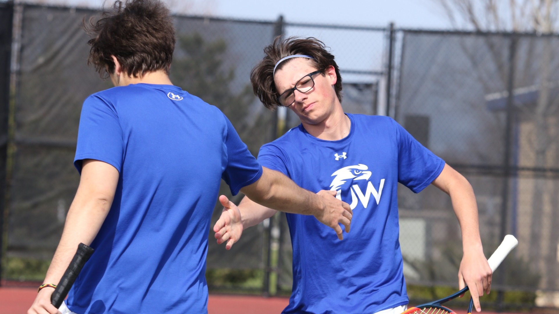 Two men's tennis players hi-fiving after a set. 
