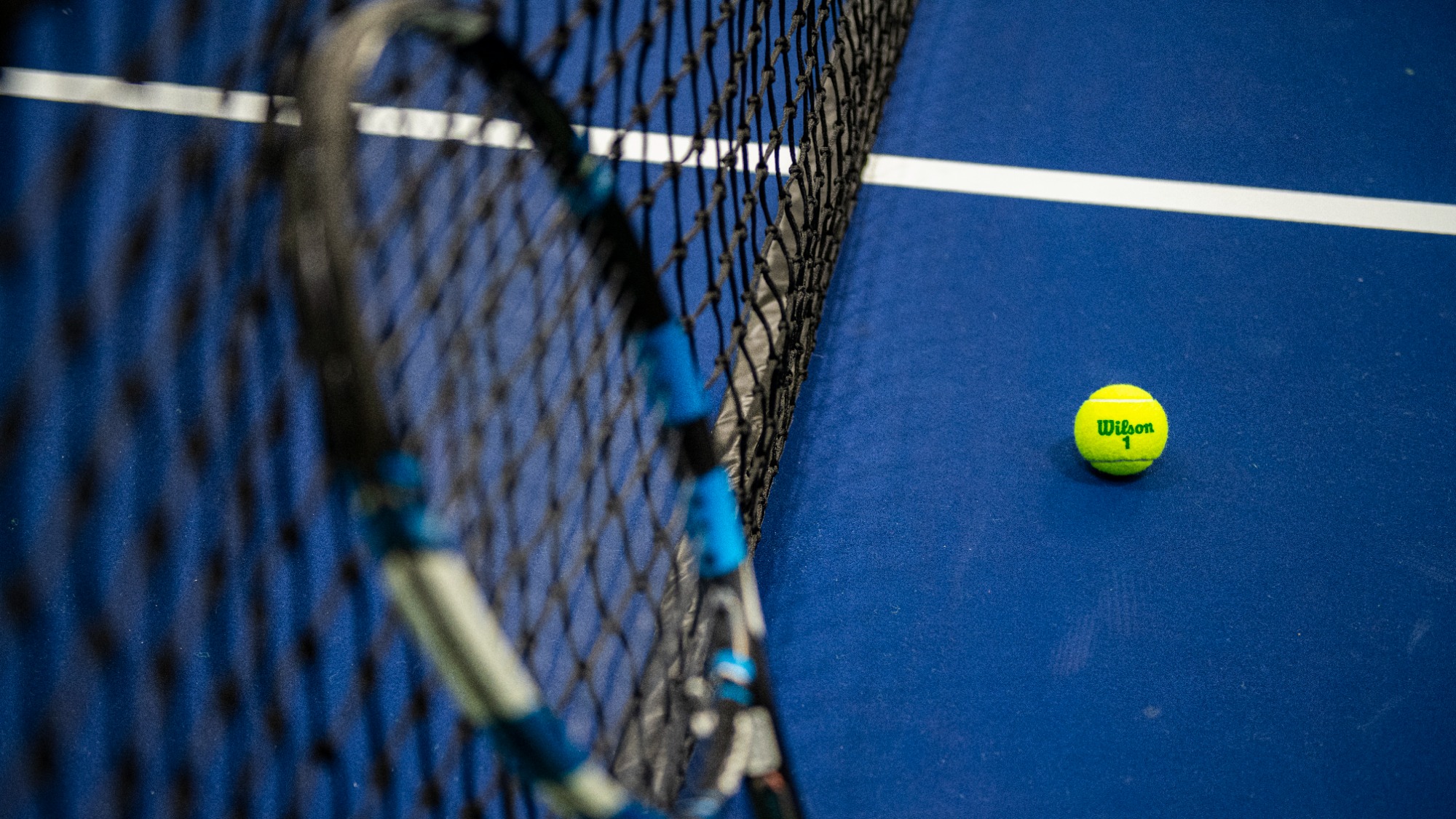 A tennis racquet stands up against the net with a tennis ball on the court