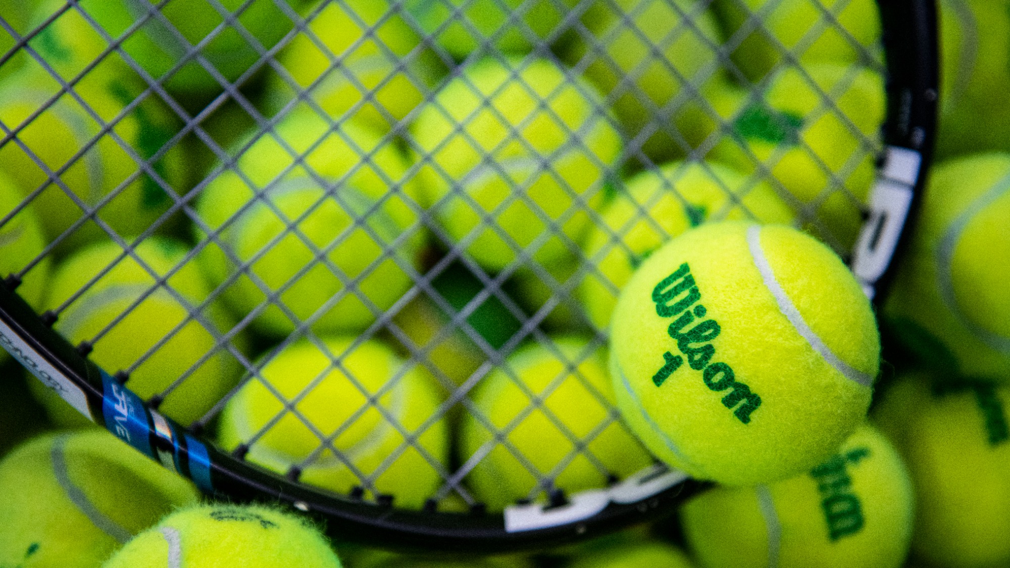 A photo of a bucket of tennis balls and a racquet