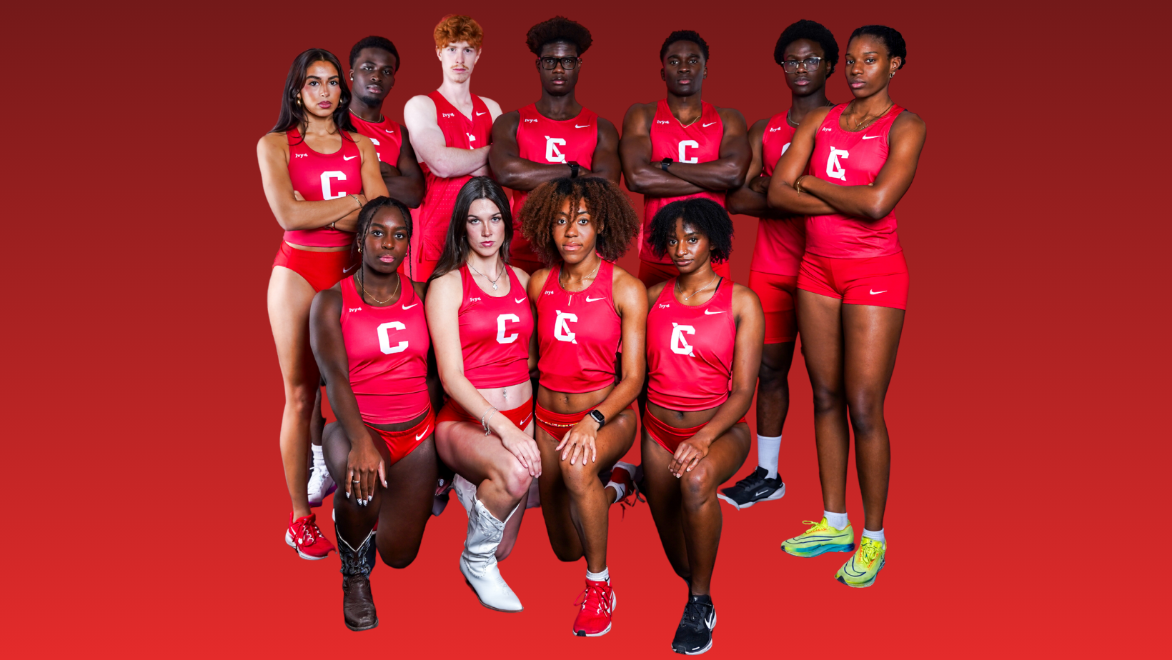 Group photo of Cornell men’s and women’s track and field athletes posing in red uniforms with a white “C,” arranged in two rows against a solid red background. Several athletes stand with arms crossed in the back row, while others kneel in front, all facing the camera.