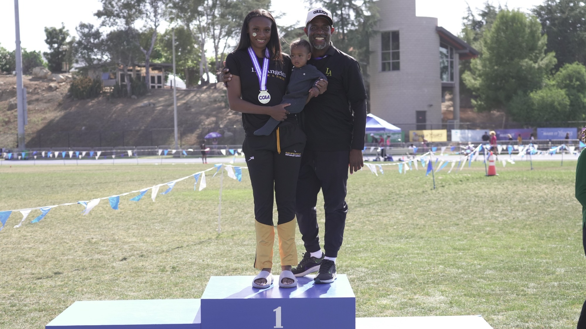 summer stevenson stands on the podium with her baby boy and assistant coach Sean Fernandes