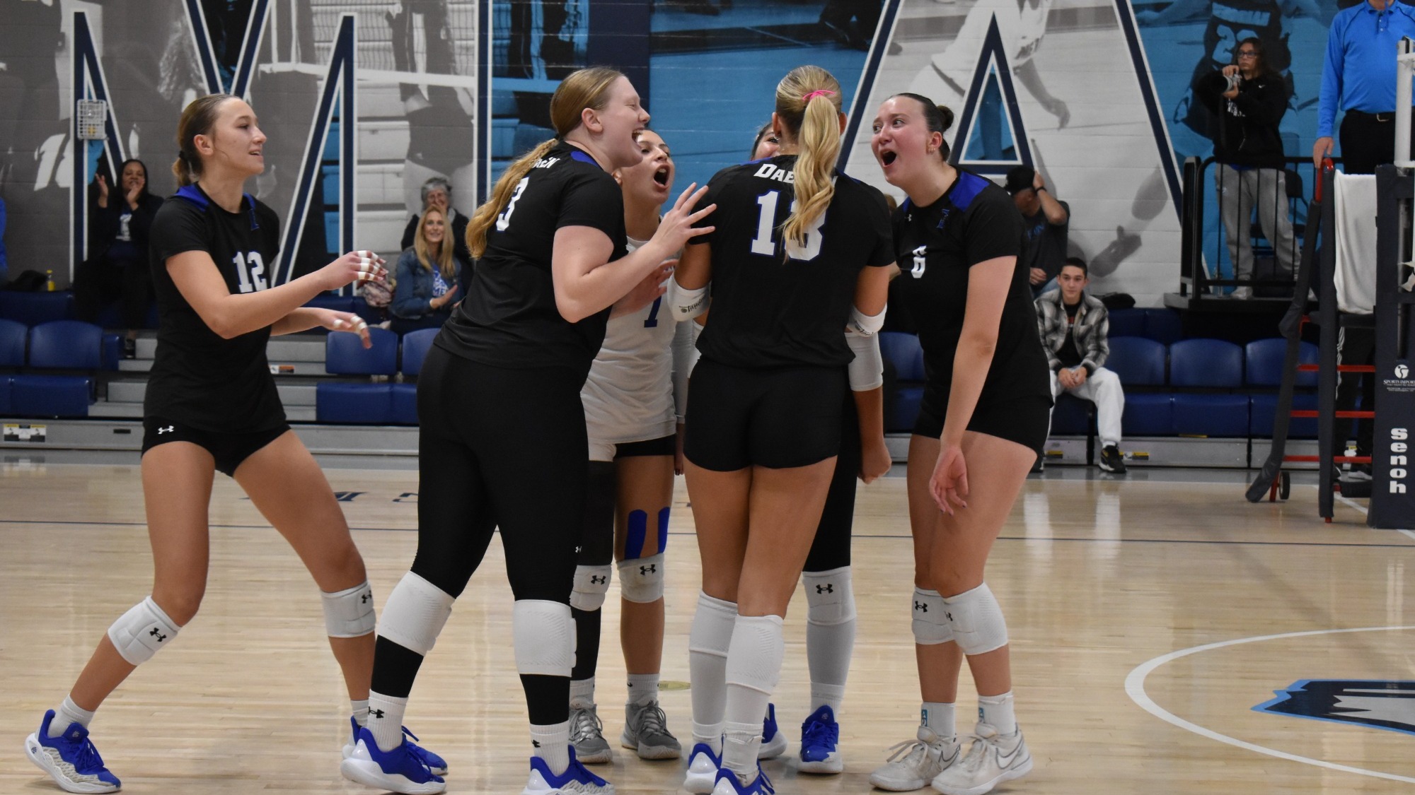 Women's volleyball players celebrate a point at the ECC Championship semifinals