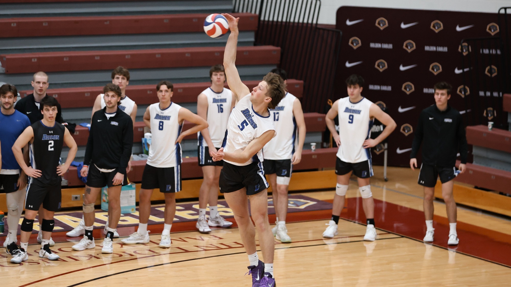 Peter Leicht serves the ball as members of his team look on from the bench area behind him