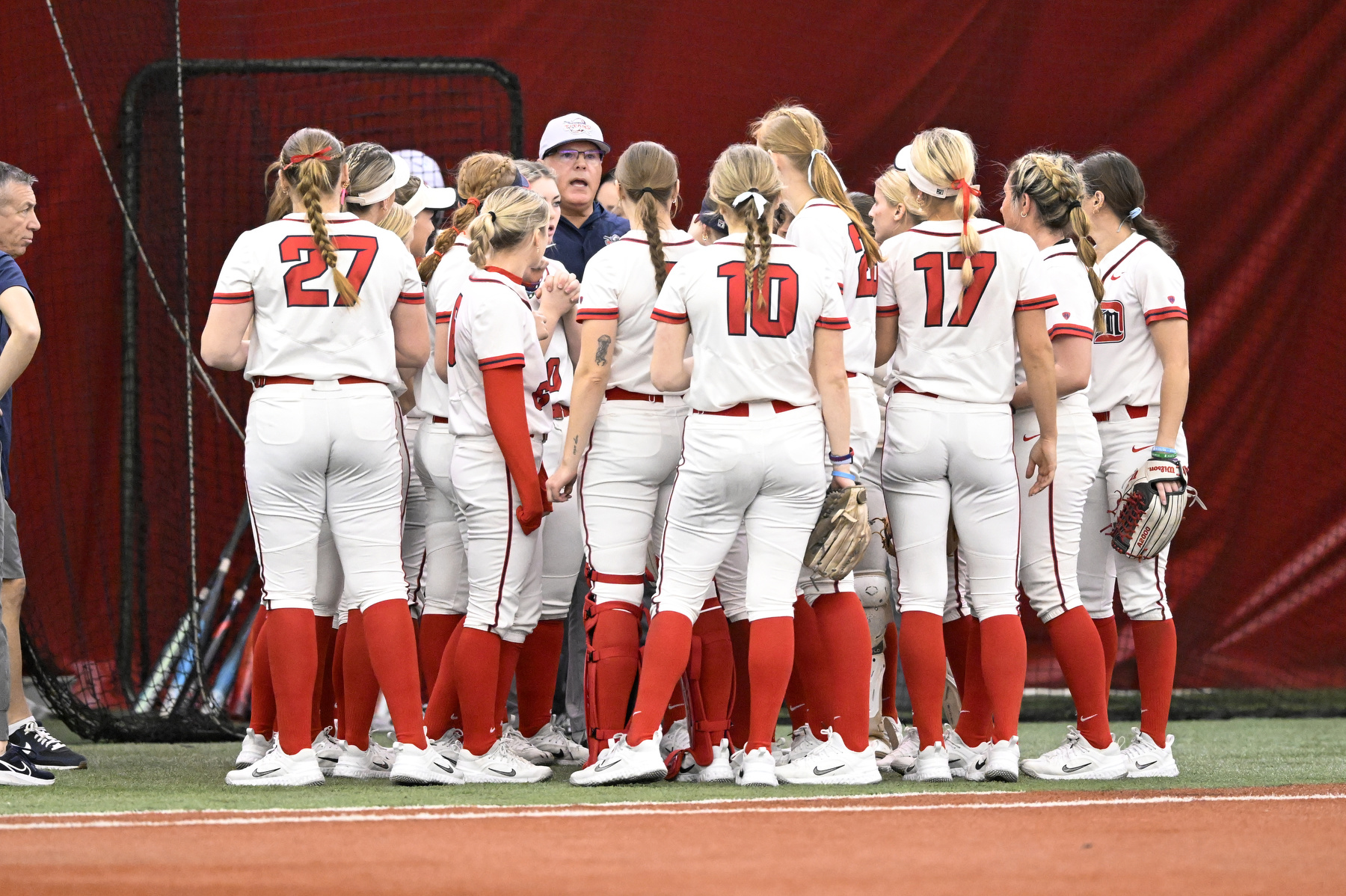 Detroit Mercy softball head coach Dan Vitale, left center background, talks to his team in between innings in a game against Drake University, Friday, February 6, 2025, at The Dome at the Parkway Bank Sports Complex in Rosemont, IL.