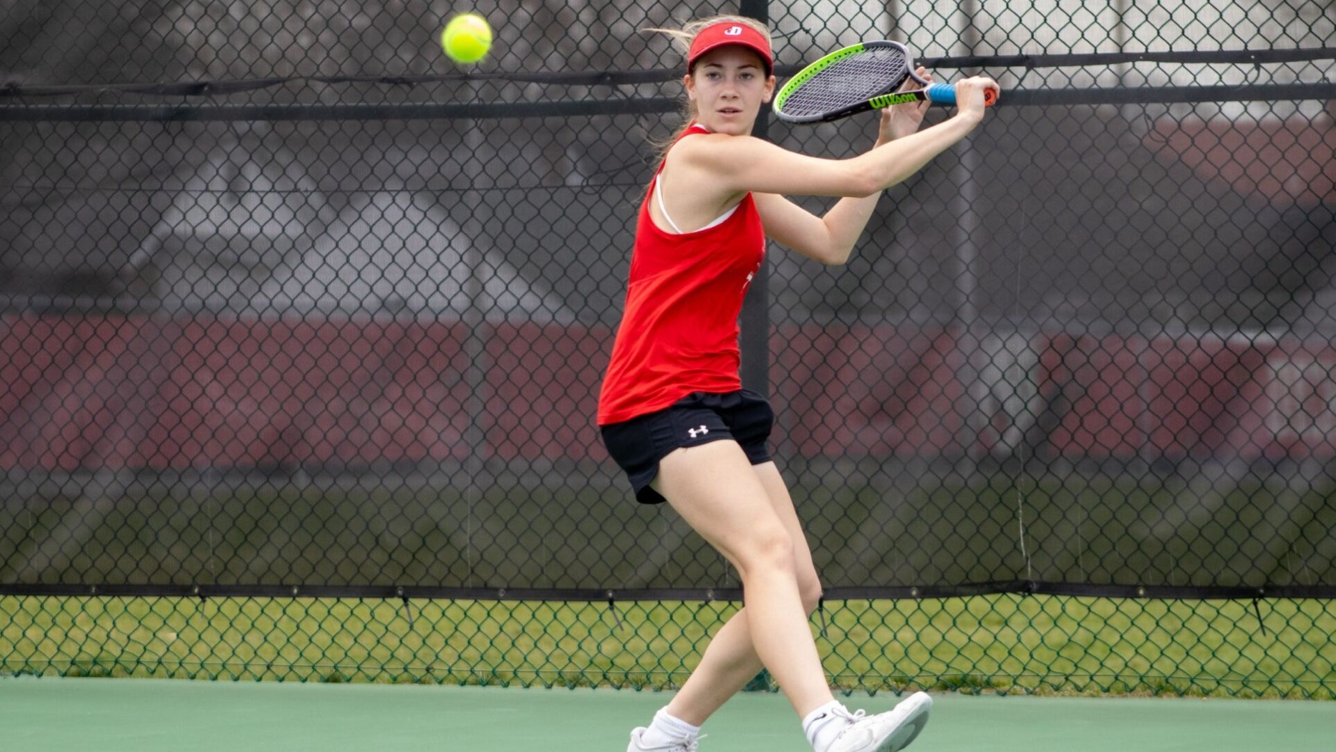 Women's tennis player going for a backhand shot against Bryn Mawr College during the 2025 spring season