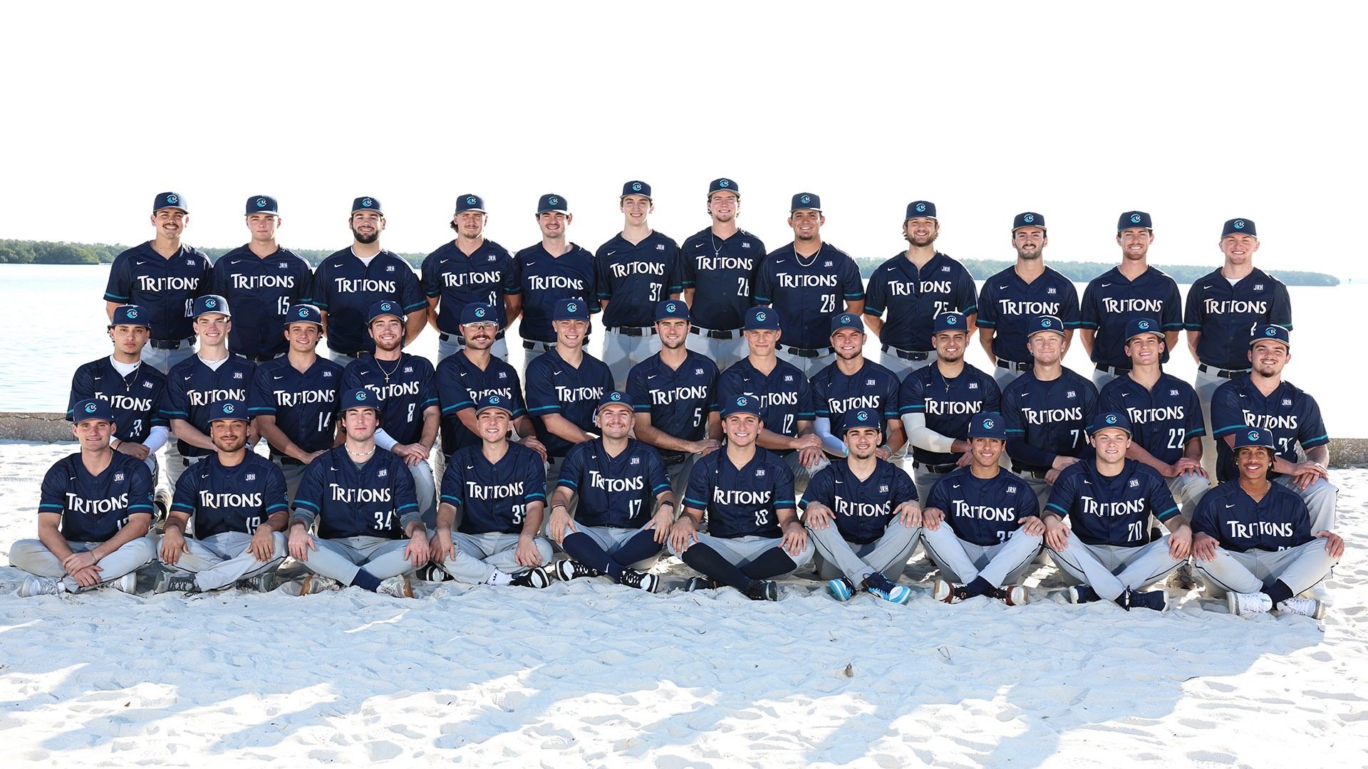 40 baseball players in three rows for a team picture on a beach with players in uniform 