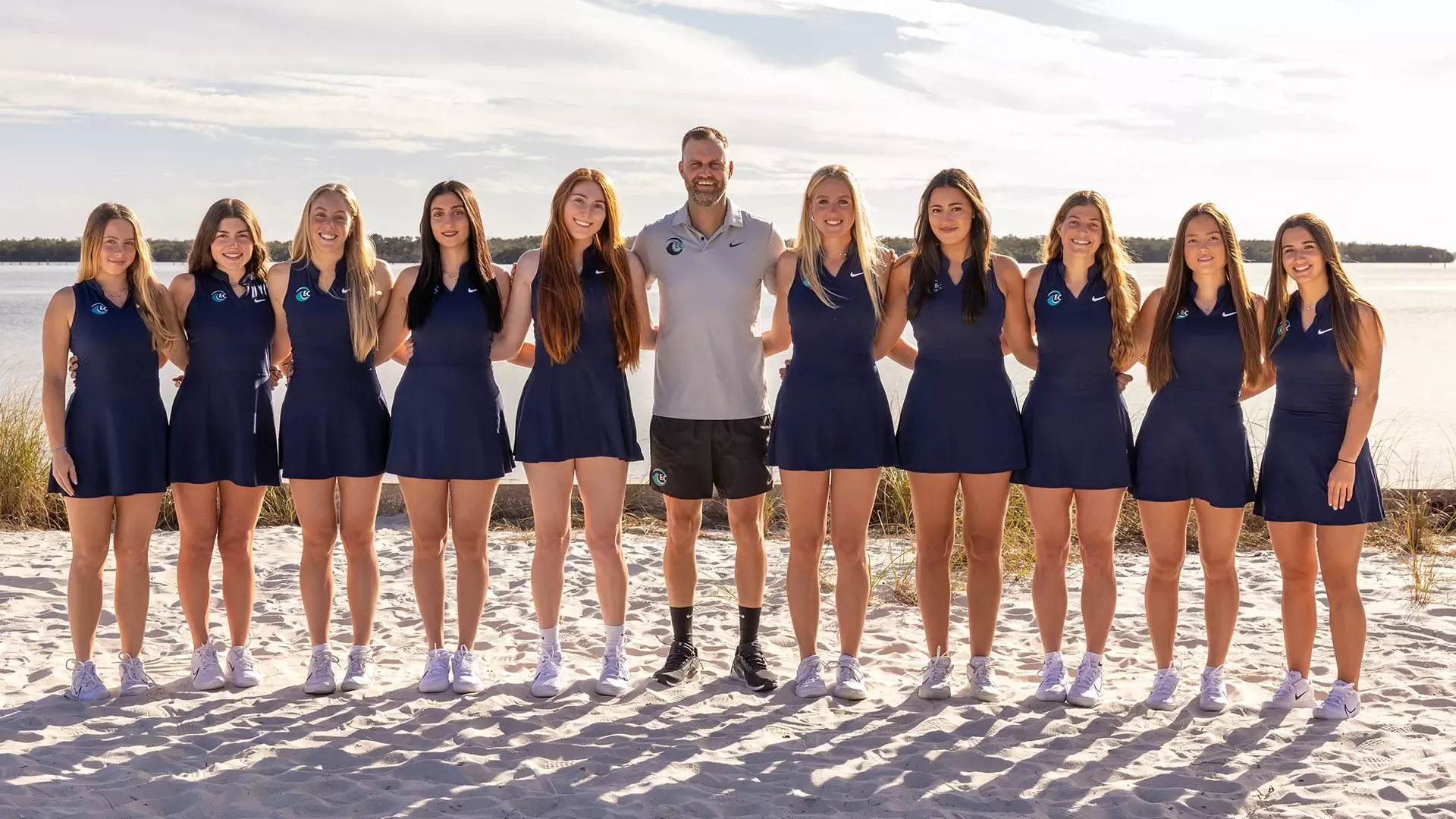 women's tennis players and coaches posed for team picture at the beach 