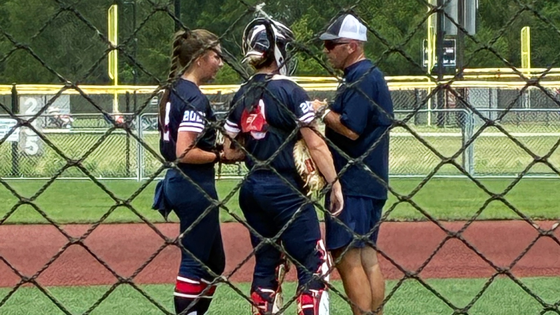 male softball coach with two players at the pitching cicle