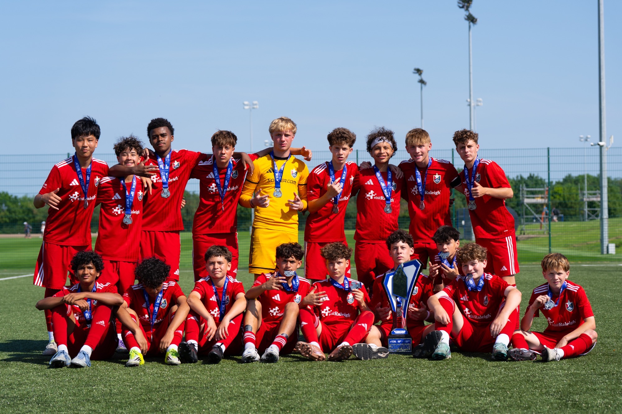 A group photo of North Carolina FC wearing medals in front of a trophy for winning the ECNL International Tournament