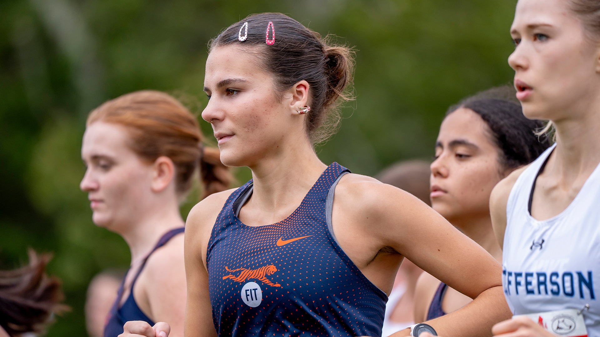 FIT women's cross country runner Anika Selover, wearing a navy blue and orange Tigers uniform, prepares for a race alongside competitors from other colleges, including Jefferson.