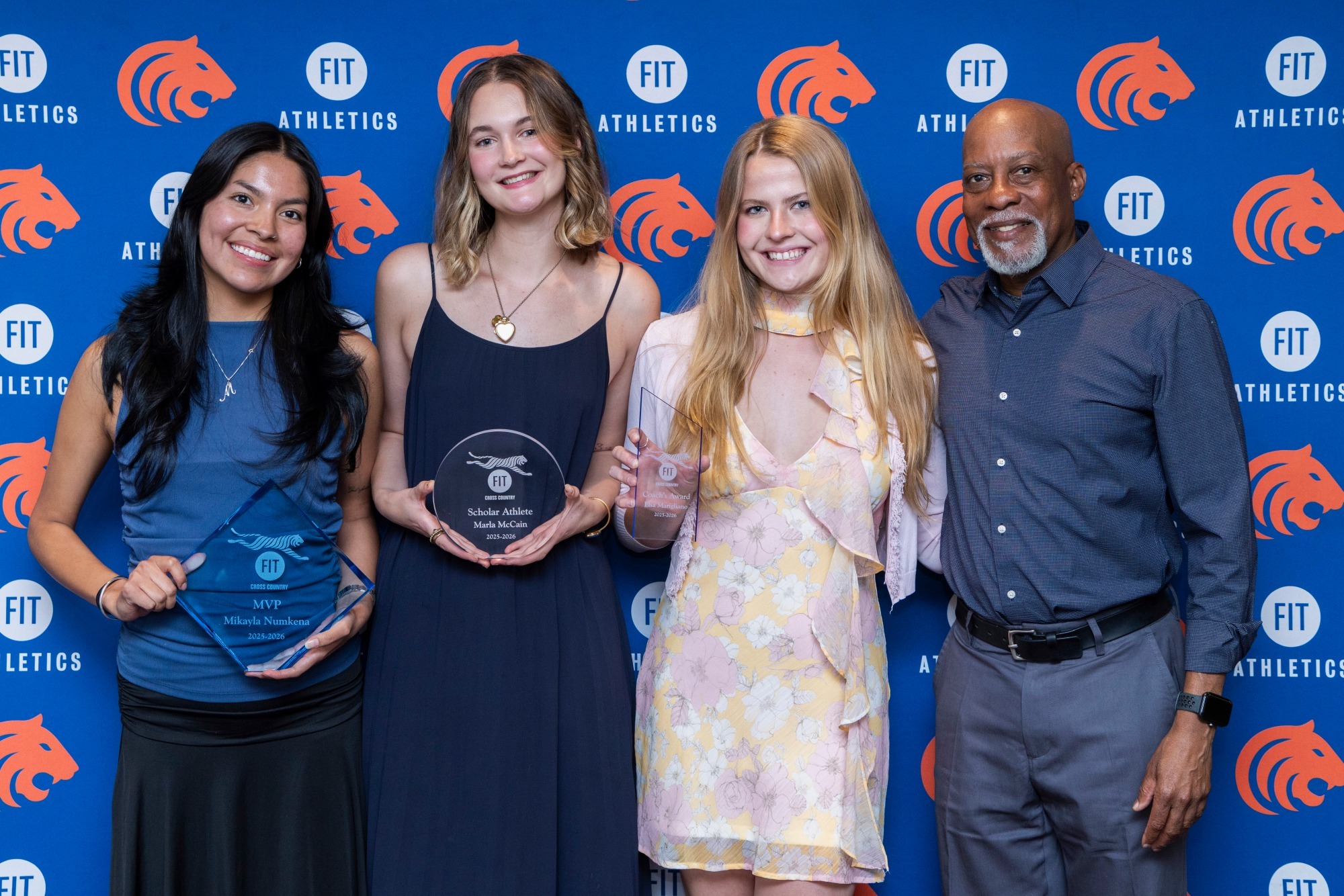 Four individuals pose in front of a FIT Athletics backdrop, with three student-athletes holding award plaques.