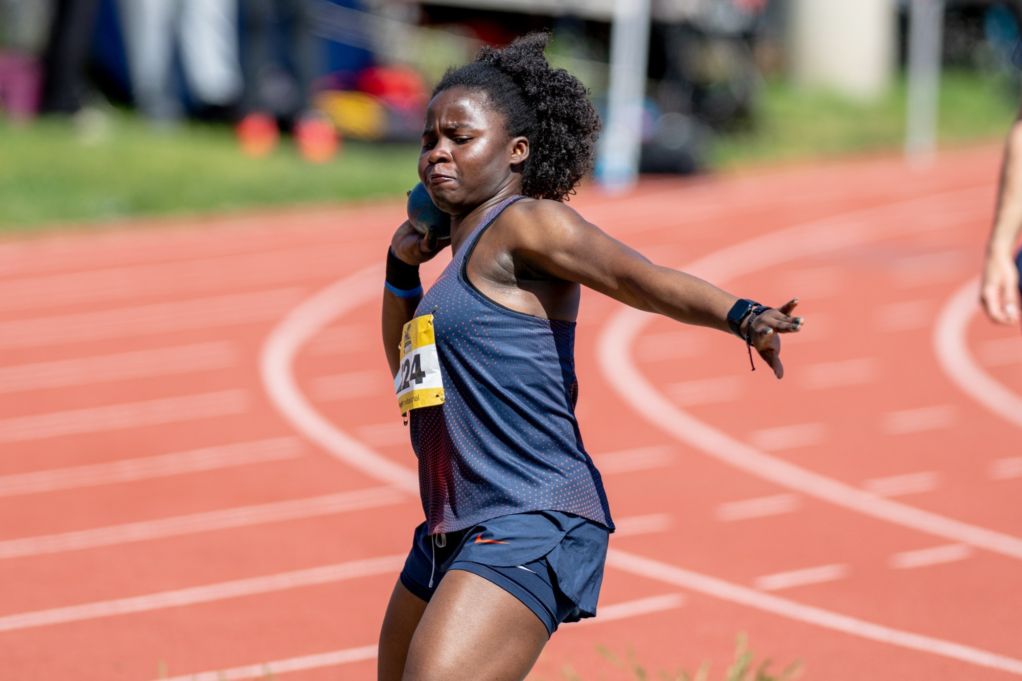 Track and field athlete preparing to release a shot put during a meet on an outdoor track.