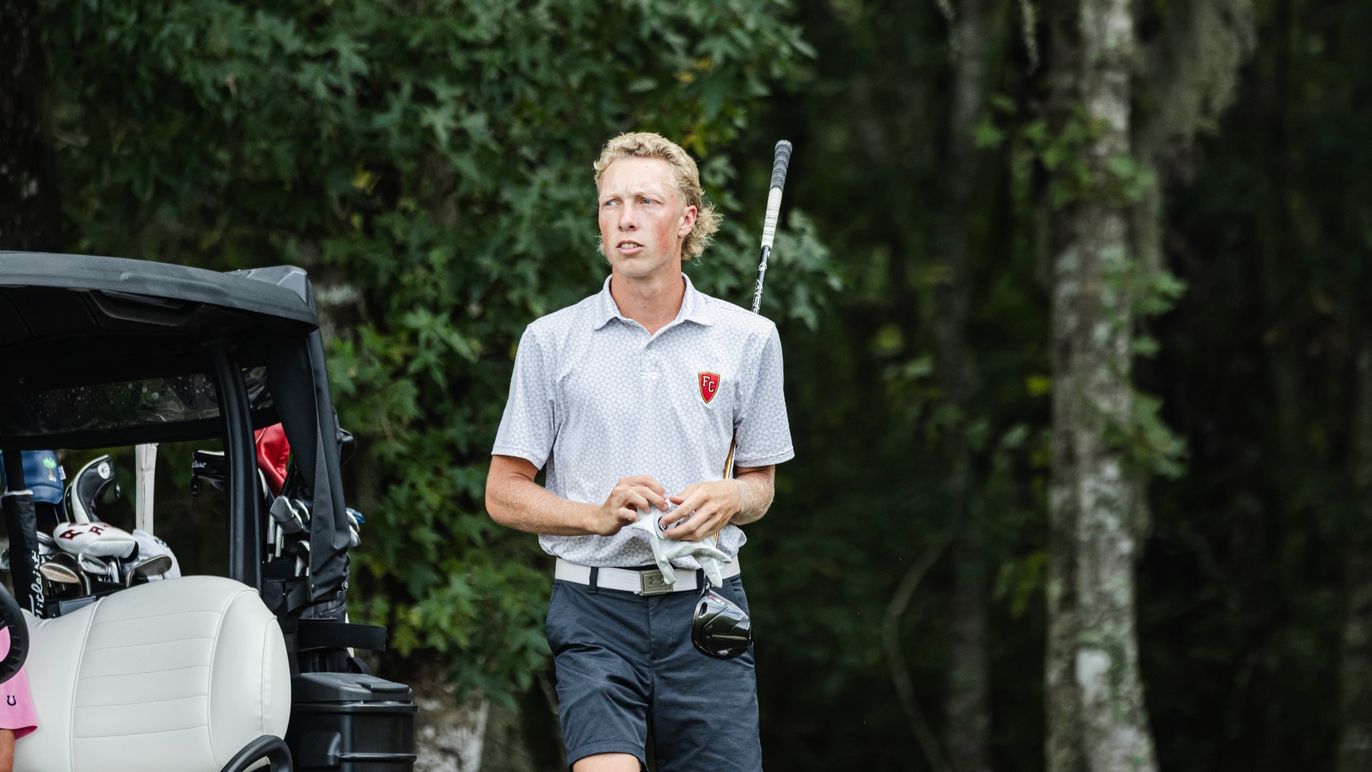Masen McKain adjusts his glove while carrying his driver to the tee box
