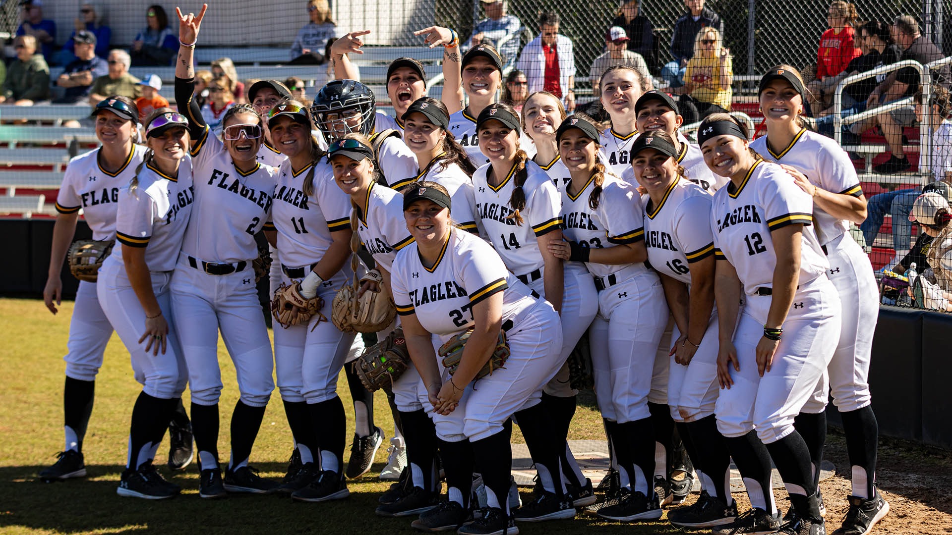 The softball team poses for a photo in front of the backstop
