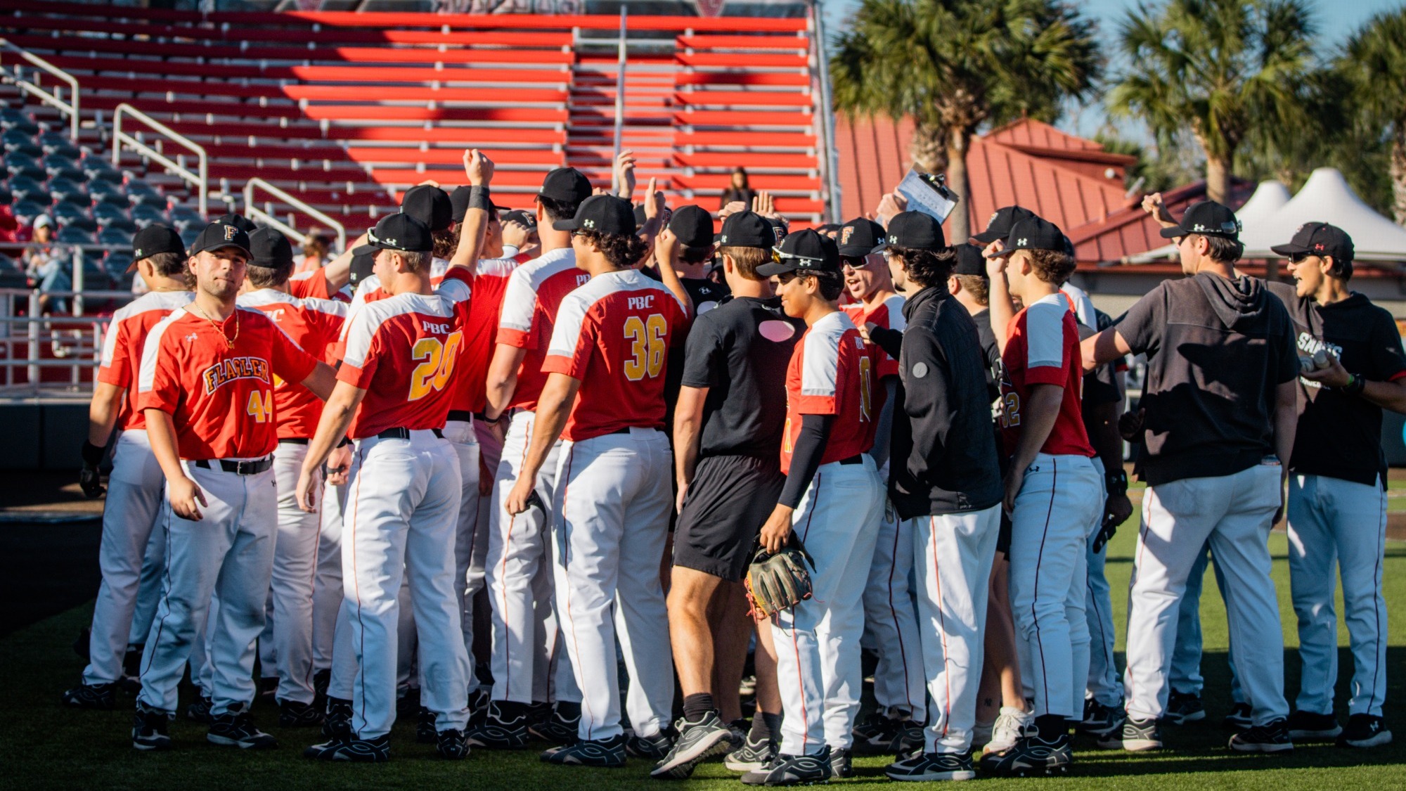 Flagler baseball players in a huddle in front of the dugout after the game