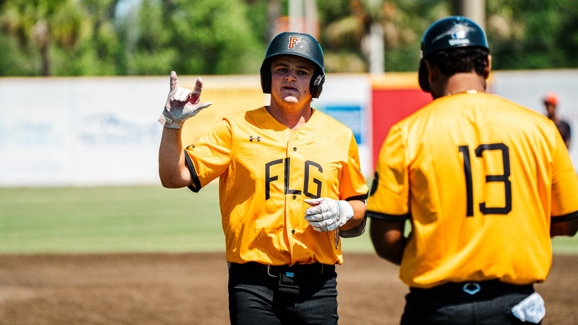 Payton Palldino raises his hand up towards the dugout after returning to first base after a hit