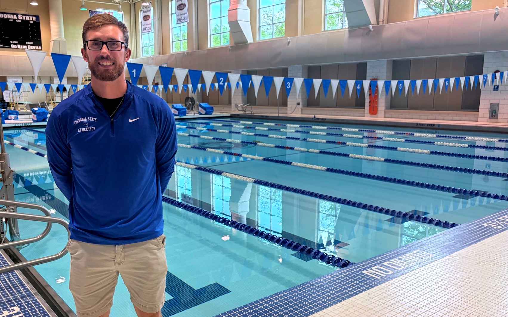 Fredonia State swimming and diving coach Ryan Kreuser in front of pool at the Steele Hall Natatorium