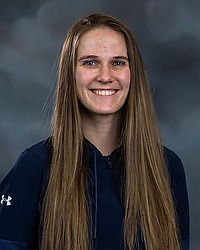 Gallaudet softball 2023 headshot Kendall Hudson. The coach is wearing a navy blue pullover.. The coach is photographed with a gray background in the back.